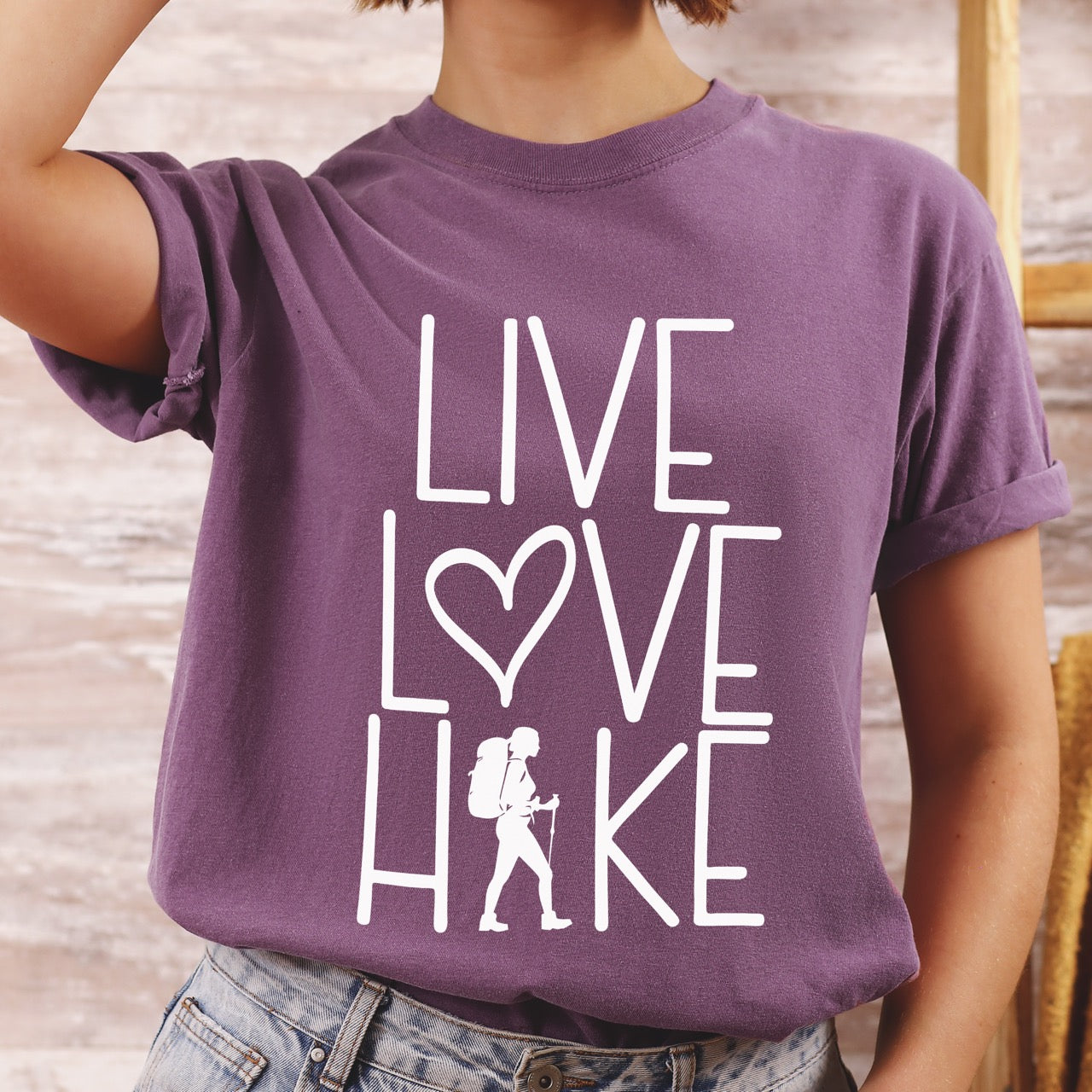 Woman wearing Women's hiking lifestyle shirt Live Love Hike with minimalist stacked typography heart symbol and female hiker silhouette on Comfort Colors tee for outdoor enthusiasts celebrating trail passion and for hikers and foodies