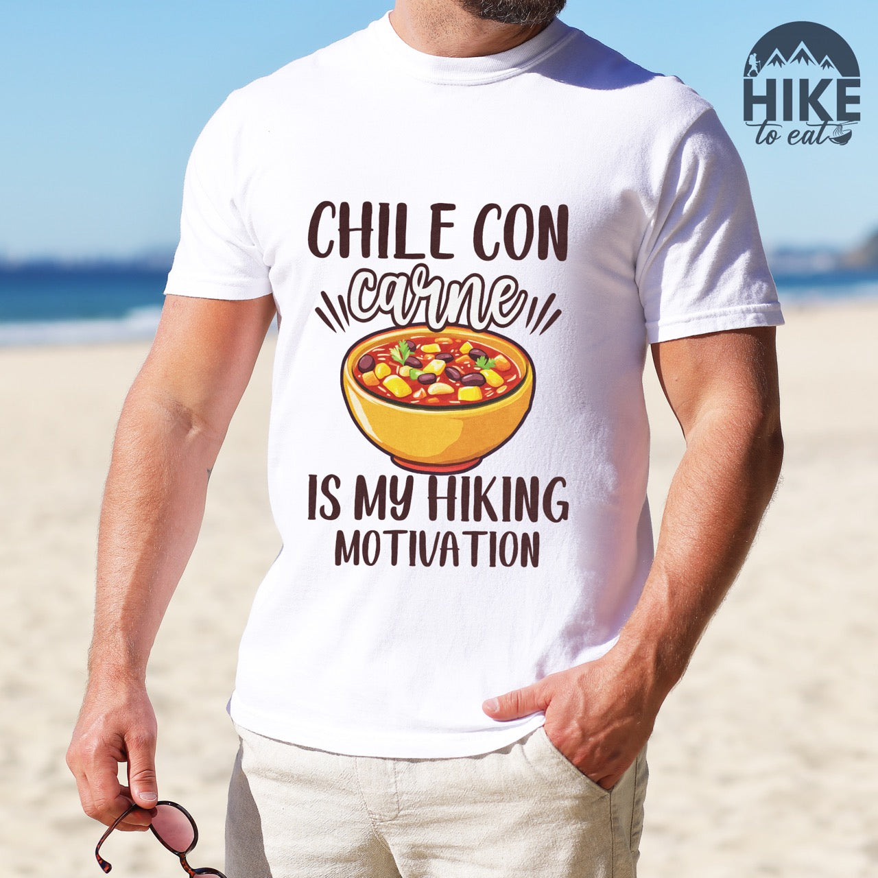Man wearing white Chile con carne is my Hiking Motivation statement tee with bold typography, script lettering, and colorful chili bowl illustration for comfort food-loving outdoor enthusiasts