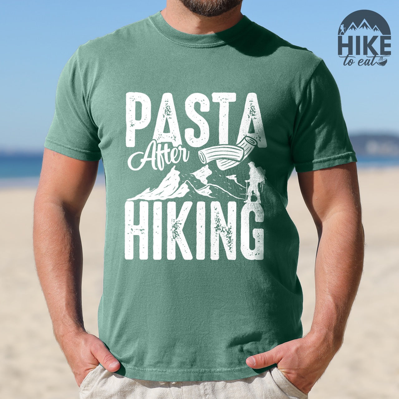 Man wearing Light green "Pasta after hiking" colored vintage tee with bold typography, birds, mountains, illustrated pieces of pasta, and backpackers for pasta lovers.