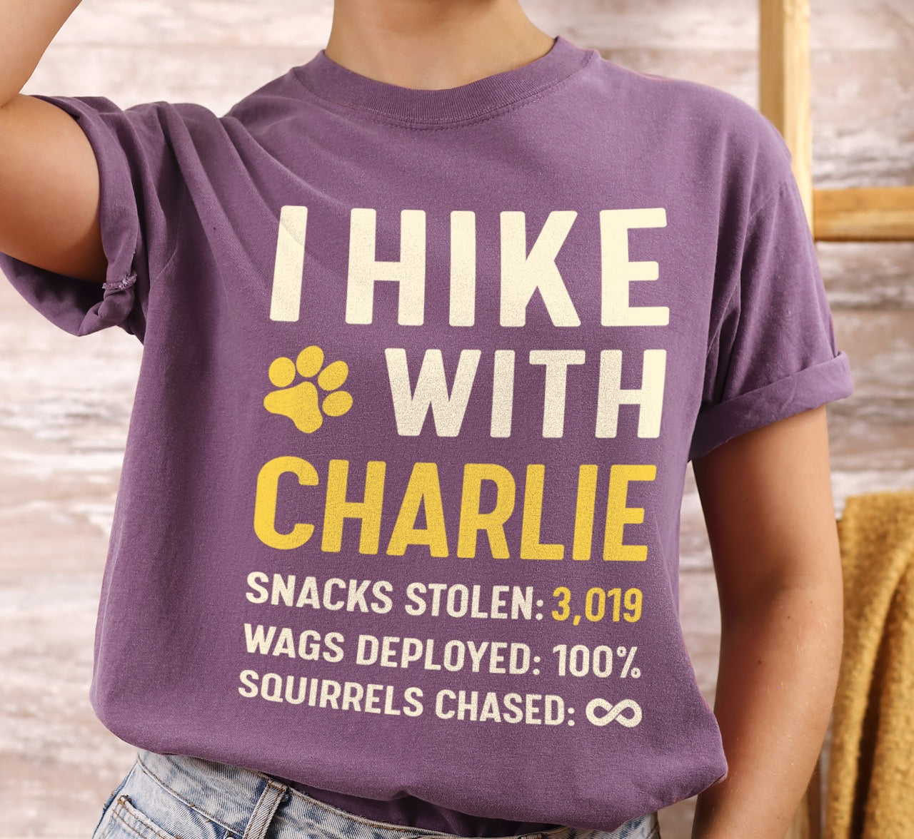 Woman wearing purple Personalized dog hiking shirt I Hike with custom pet name of Charlie featuring paw print graphic, funny adventure statistics including snacks stolen of 3,019, wags deployed and squirrels chased on Comfort Colors tee for outdoor pet lovers