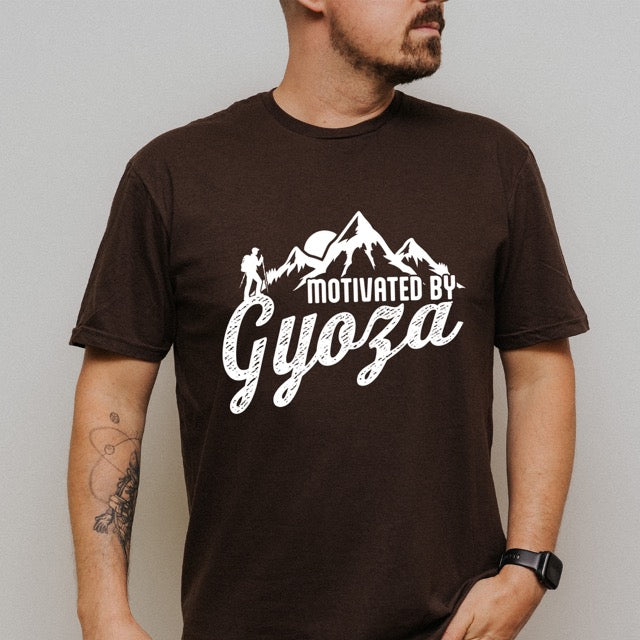 Man wearing Dark Chocolate (brown) Motivated by Gyoza statement tee with distressed typography, mountain peaks, and hiker silhouette for gyoza lovers and japanese food lovers.