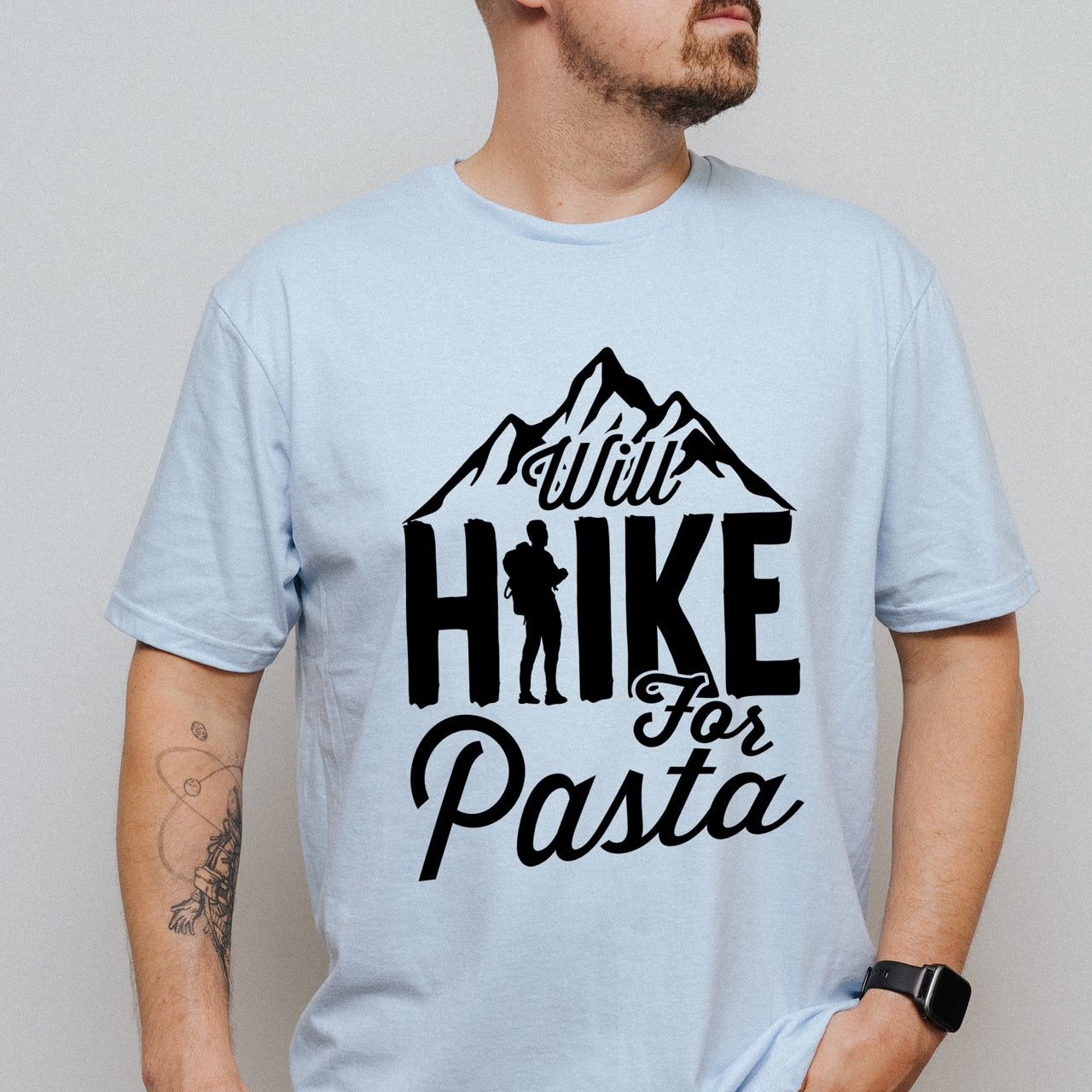 man wearing light blue Will Hike for Pasta statement tee with bold typography, mountain peaks, and backpacker silhouette for pasta devotees and hikers