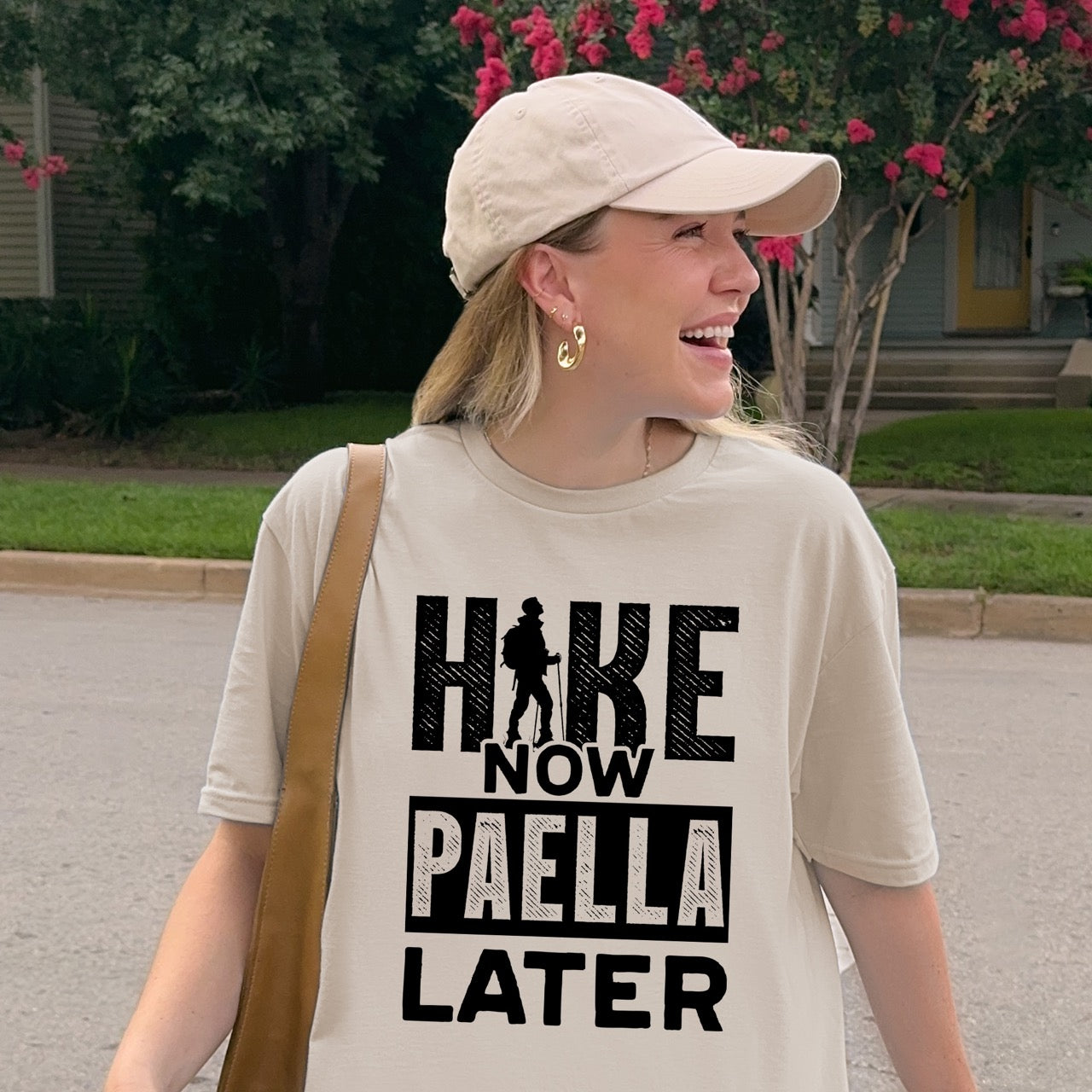 woman wearing sand (beige) Hike Now Paella Later statement tee with bold distressed typography and hiker silhouette for Spanish food-loving outdoor enthusiasts and hikers