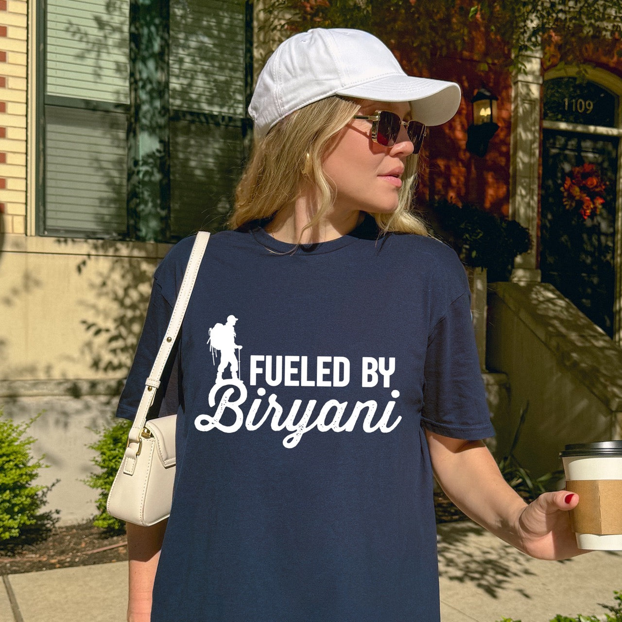 woman wearing Navy Fueled by Biryani statement tee with bold typography, elegant script lettering, and hiker silhouette for Indian food-loving outdoor enthusiasts, foodies and hikers