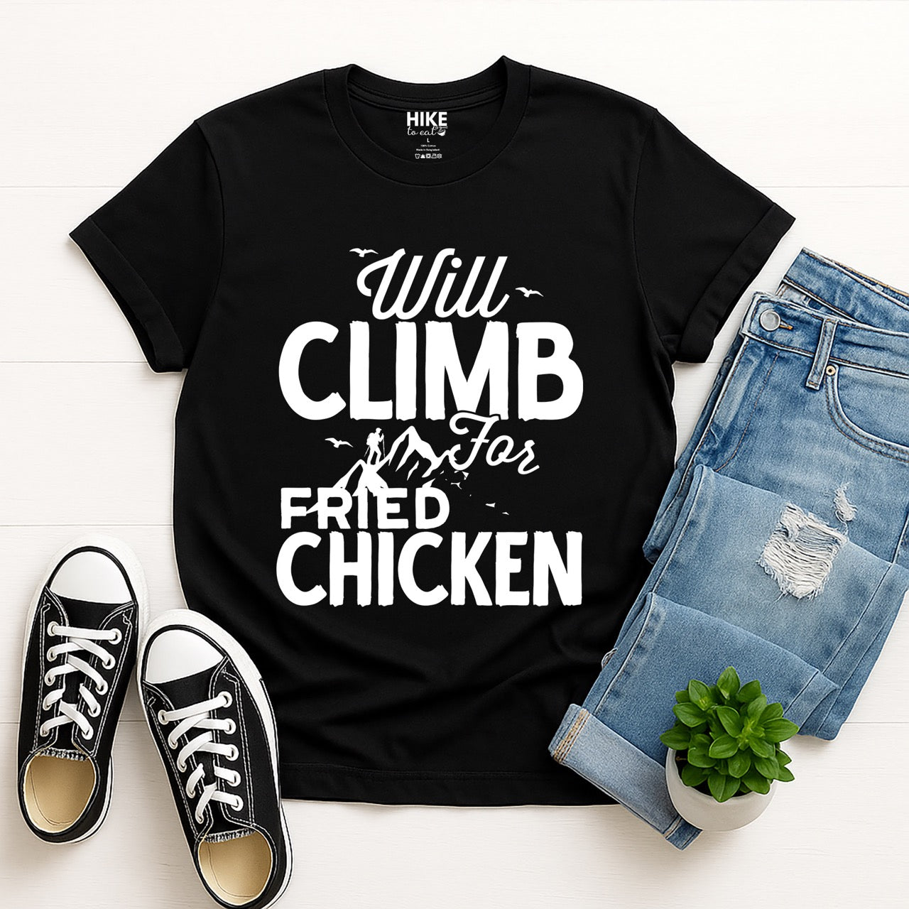 Black Will climb for Fried Chicken statement tee with bold and script typography, mountain peaks, climber silhouette, and flying birds for chicken-loving outdoor athletes, climbers, hikers and foodies laid flat with jeans and shoes