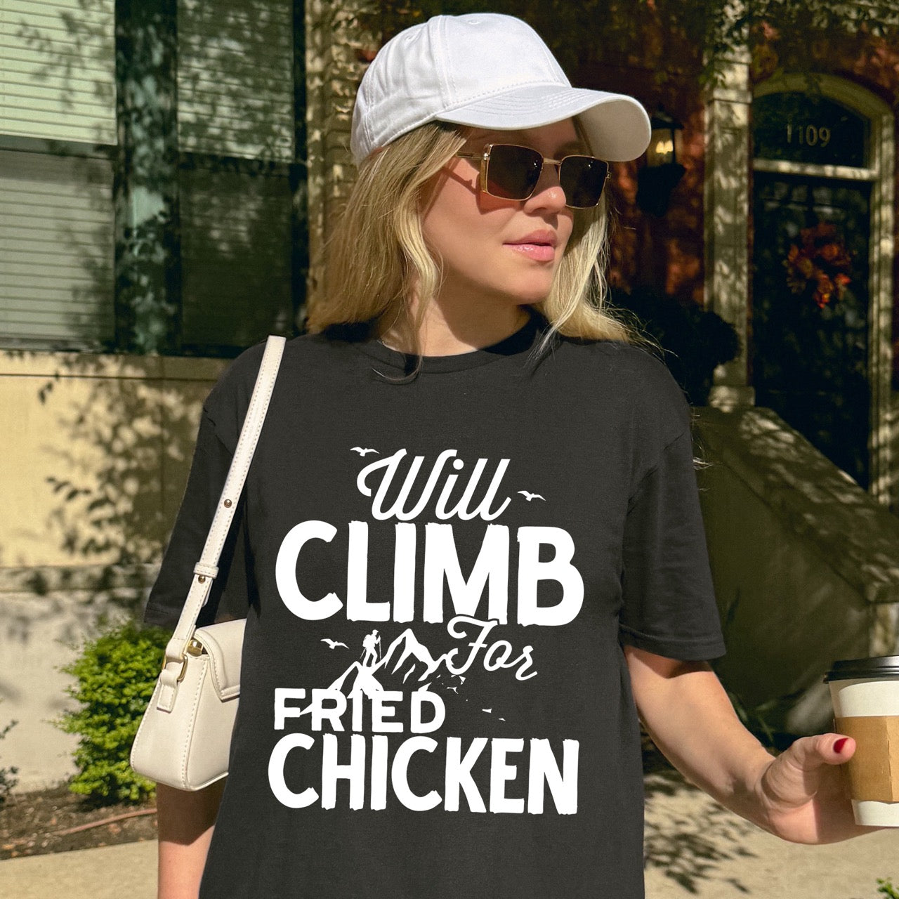 Woman wearing Black Will climb for Fried Chicken statement tee with bold and script typography, mountain peaks, climber silhouette, and flying birds for chicken-loving outdoor athletes, climbers, hikers and foodies
