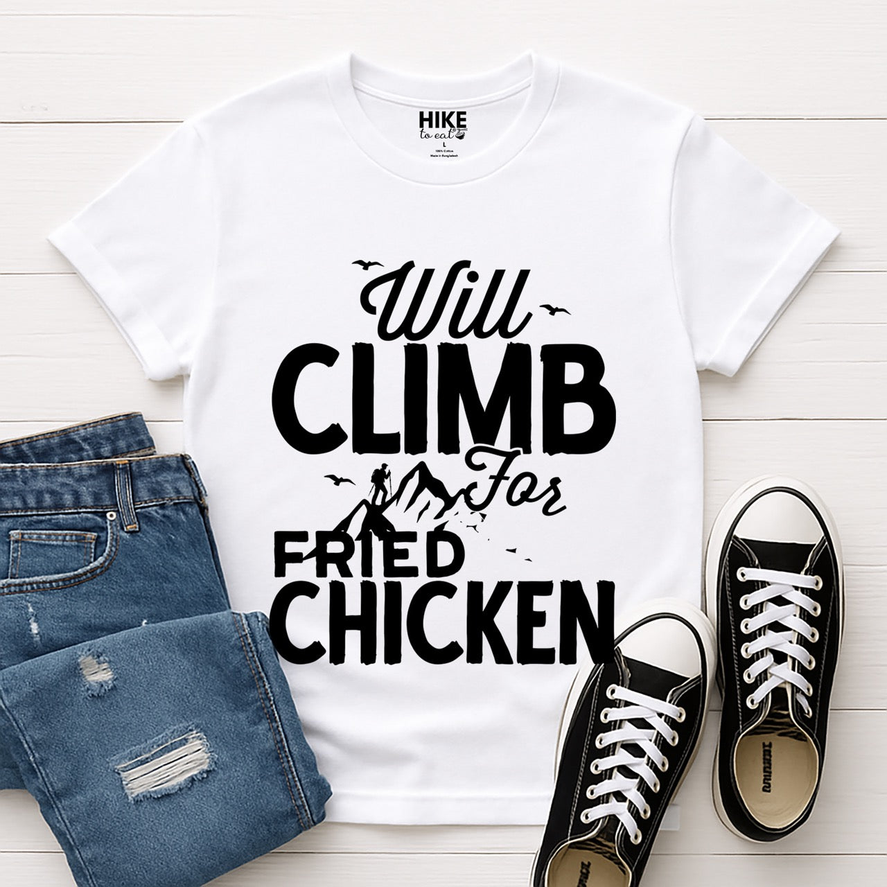 White Will climb for Fried Chicken statement tee with bold and script typography, mountain peaks, climber silhouette, and flying birds for chicken-loving outdoor athletes, climbers, hikers and foodies laid flat with shoes and pants