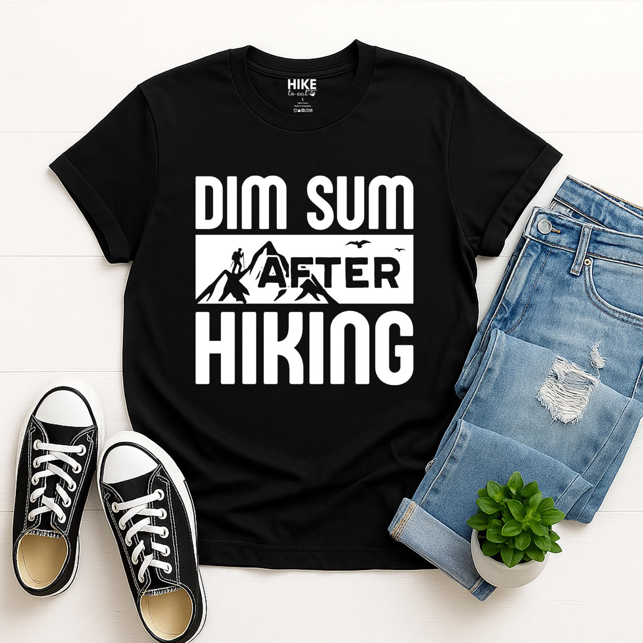 BLACK Dim Sum after Hiking statement tee with bold typography, mountain peaks, hiker silhouette, and flying birds for Chinese food-loving outdoor enthusiasts, hikers and foodies laid flat with jeans and shoes