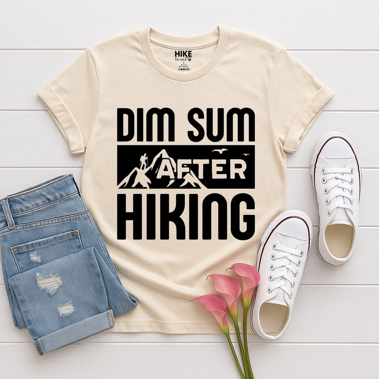 Natural (beige) Dim Sum after Hiking statement tee with bold typography, mountain peaks, hiker silhouette, and flying birds for Chinese food-loving outdoor enthusiasts, hikers and foodies laid flat with shoes and pants