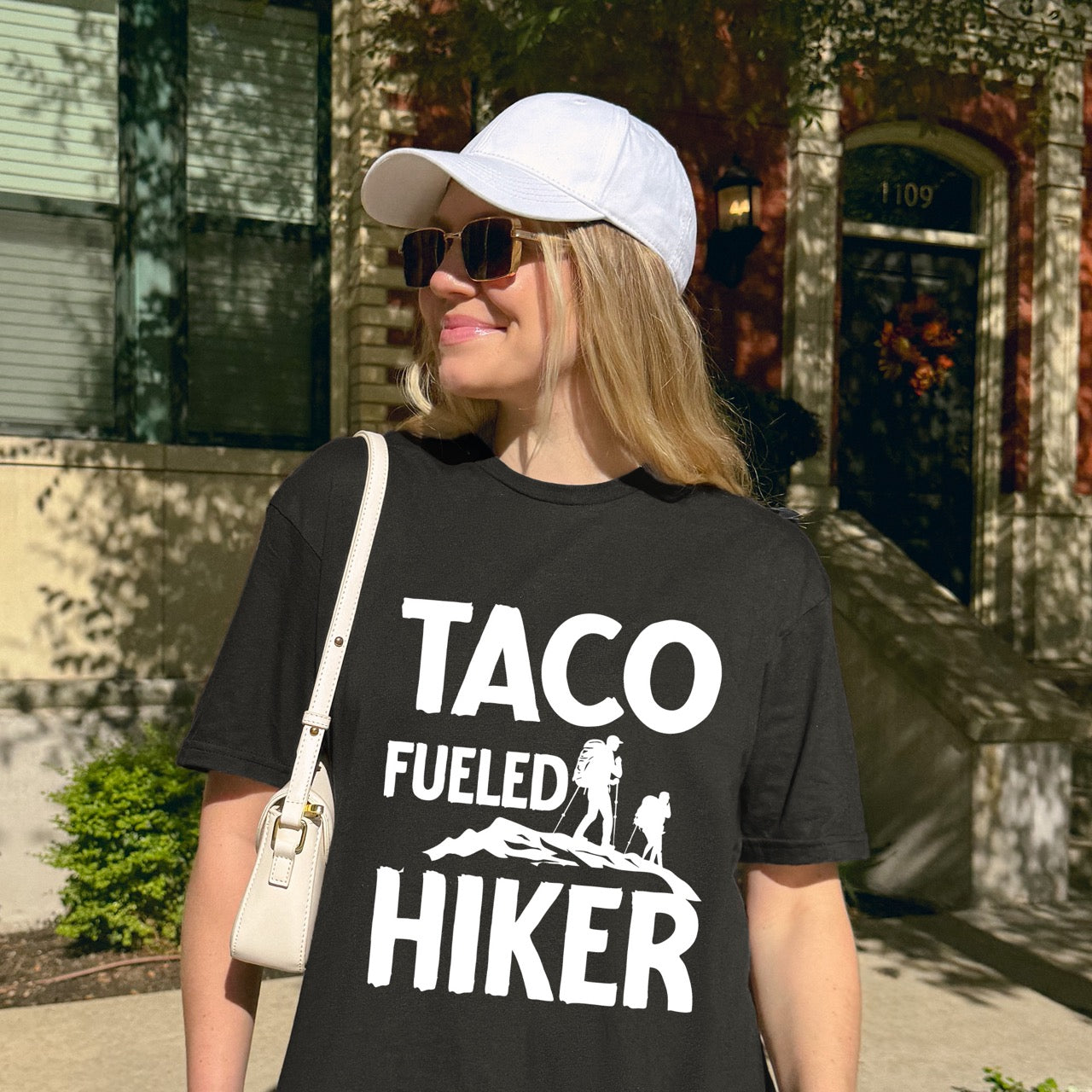 Woman wearing Black Taco Fueled Hiker statement tee with bold distressed typography and two hiker silhouettes on mountain ridge for Mexican food-loving outdoor enthusiasts, hikers and foodies