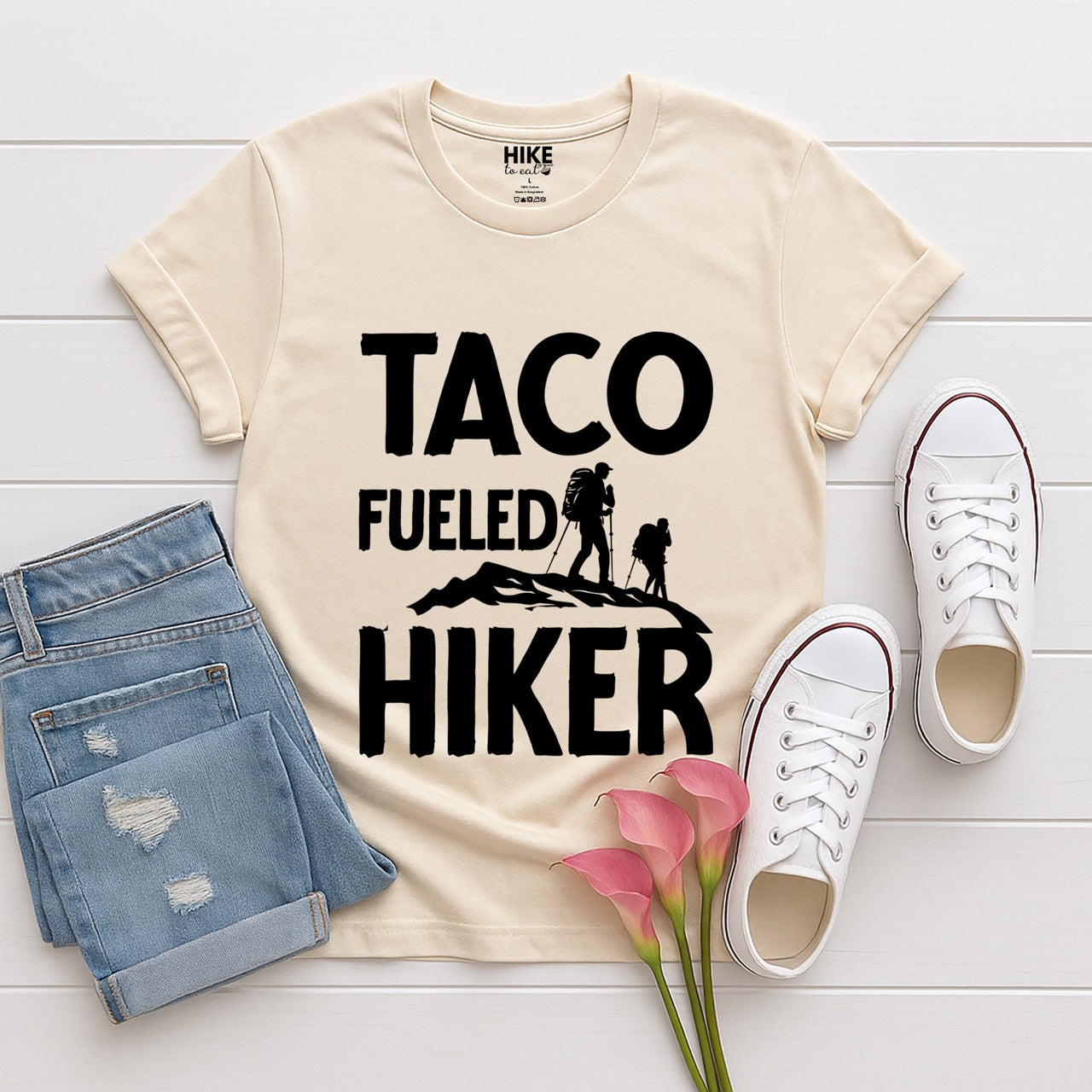 Natural (beige) Royal blue Taco Fueled Hiker statement tee with bold distressed typography and two hiker silhouettes on mountain ridge for Mexican food-loving outdoor enthusiasts, hikers and foodies laid flat with shoes and jeans