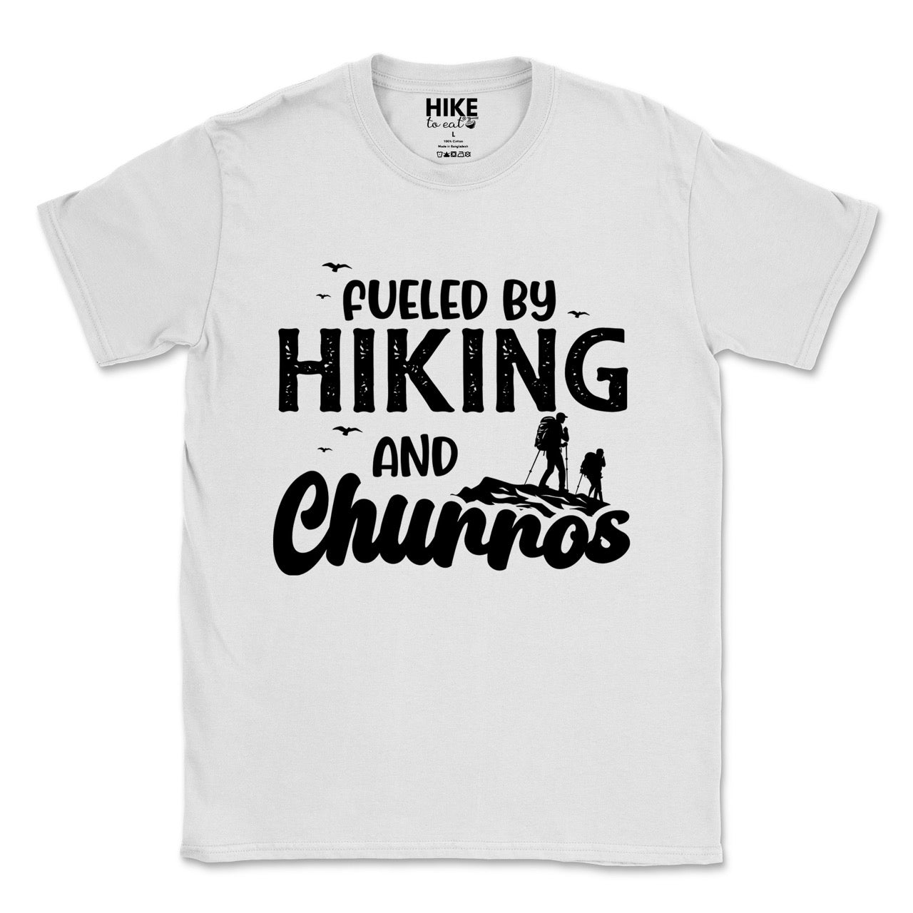 White Fueled by Hiking and Churros statement tee with bold distressed typography, flying birds, and two hiker silhouettes on mountain ridge for Spanish dessert-loving outdoor enthusiasts, hikers and foodies