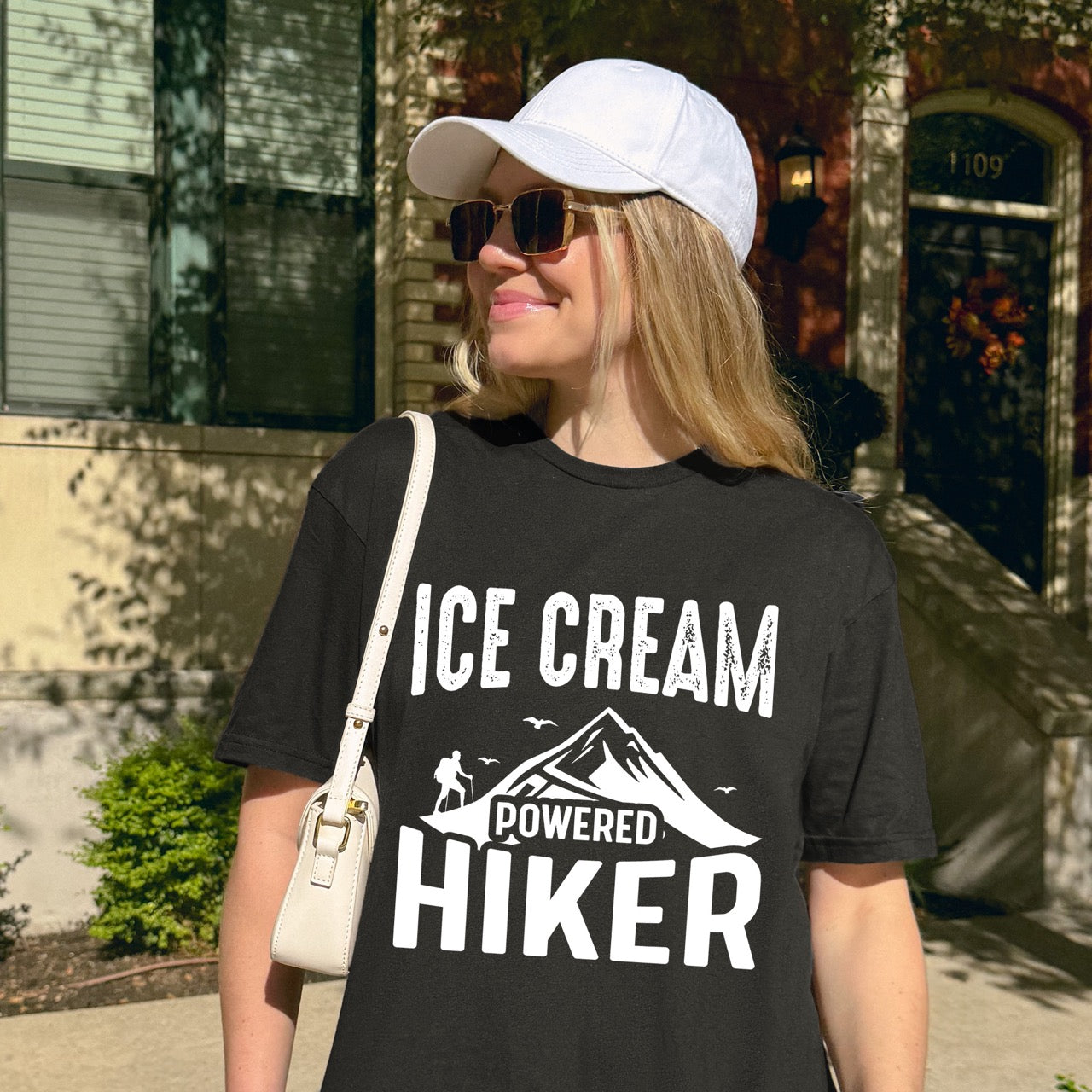 Woman wearing Black Ice Cream Powered Hiker statement tee with bold distressed typography, mountain peaks, hiker silhouette, and flying birds for dessert-loving outdoor enthusiasts, hikers and foodies