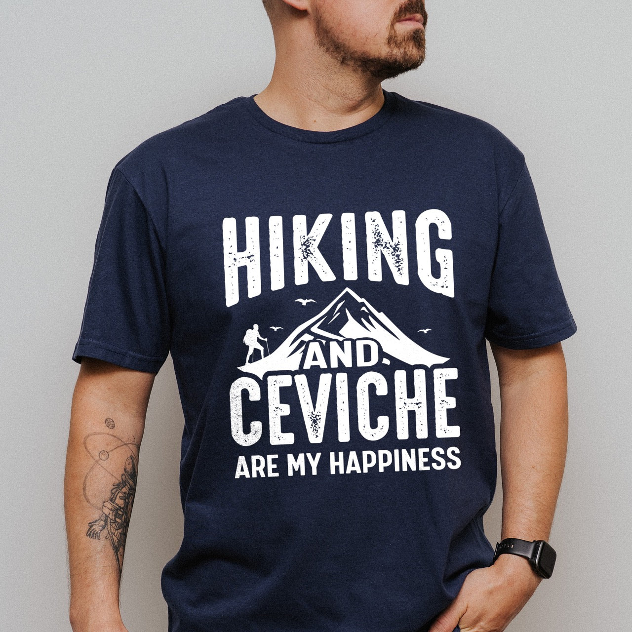 Man wearing Navy Hiking and Ceviche are my Happiness statement tee with distressed bold typography, mountain peaks, hiker silhouette, and flying birds for seafood-loving outdoor enthusiasts, foodies and hikers