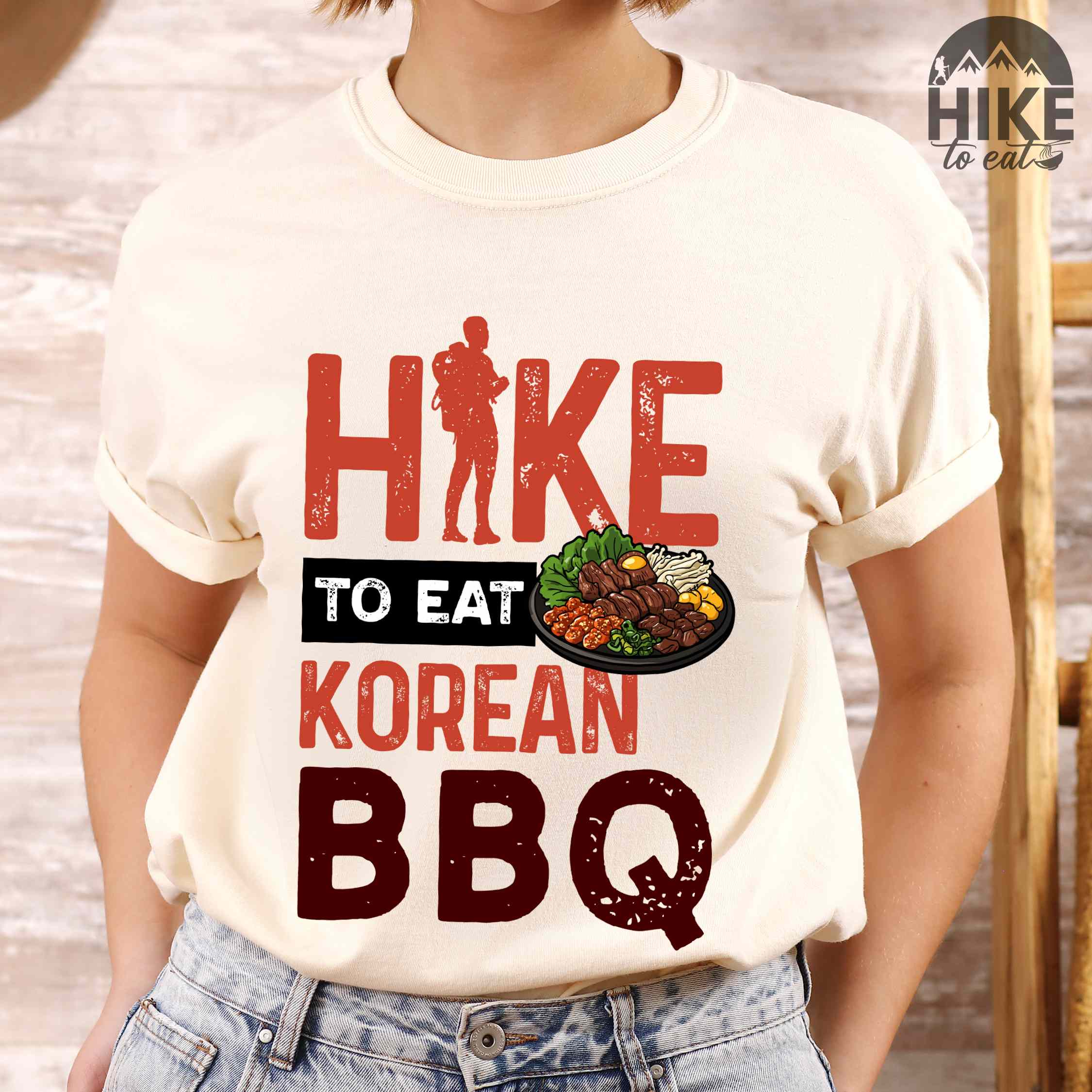 Woman wearing ivory "Hike to eat Korean bbq" colored vintage tee with bold typography, illustrated grilling platter korean bbq, mountains, birds, and backpacker for kbbq lovers.