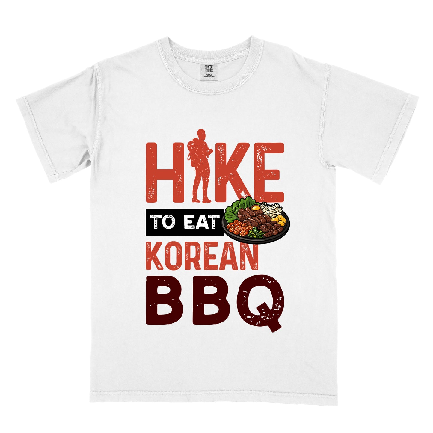 White t-shirt with red and dark red distressed text reading "HIKE TO EAT KOREAN BBQ". "HIKE" appears in large red letters at the top with a red hiker silhouette integrated into the letter "I", "TO EAT" in white text on a black rectangular background in the middle, "KOREAN" in red, and "BBQ" in dark red at the bottom. Features an illustration of Korean barbecue with meat and vegetables on a black plate extending from the black background.