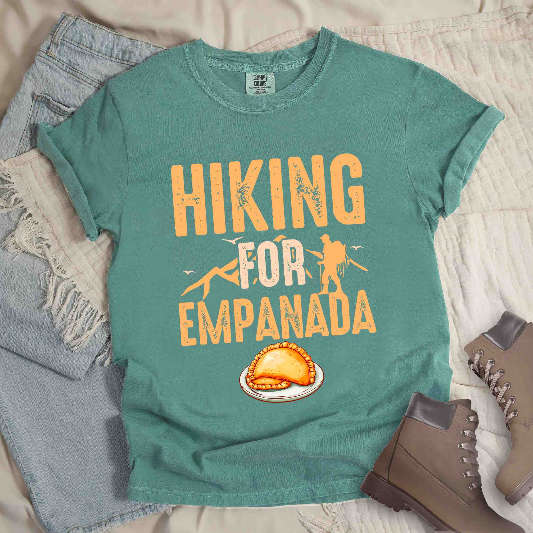 Light green "Hiking for empanada" colored vintage tee with bold typography, illustrated freshly baked empanada, mountains, birds, and backpackers for asian cuisine enthusiasts.