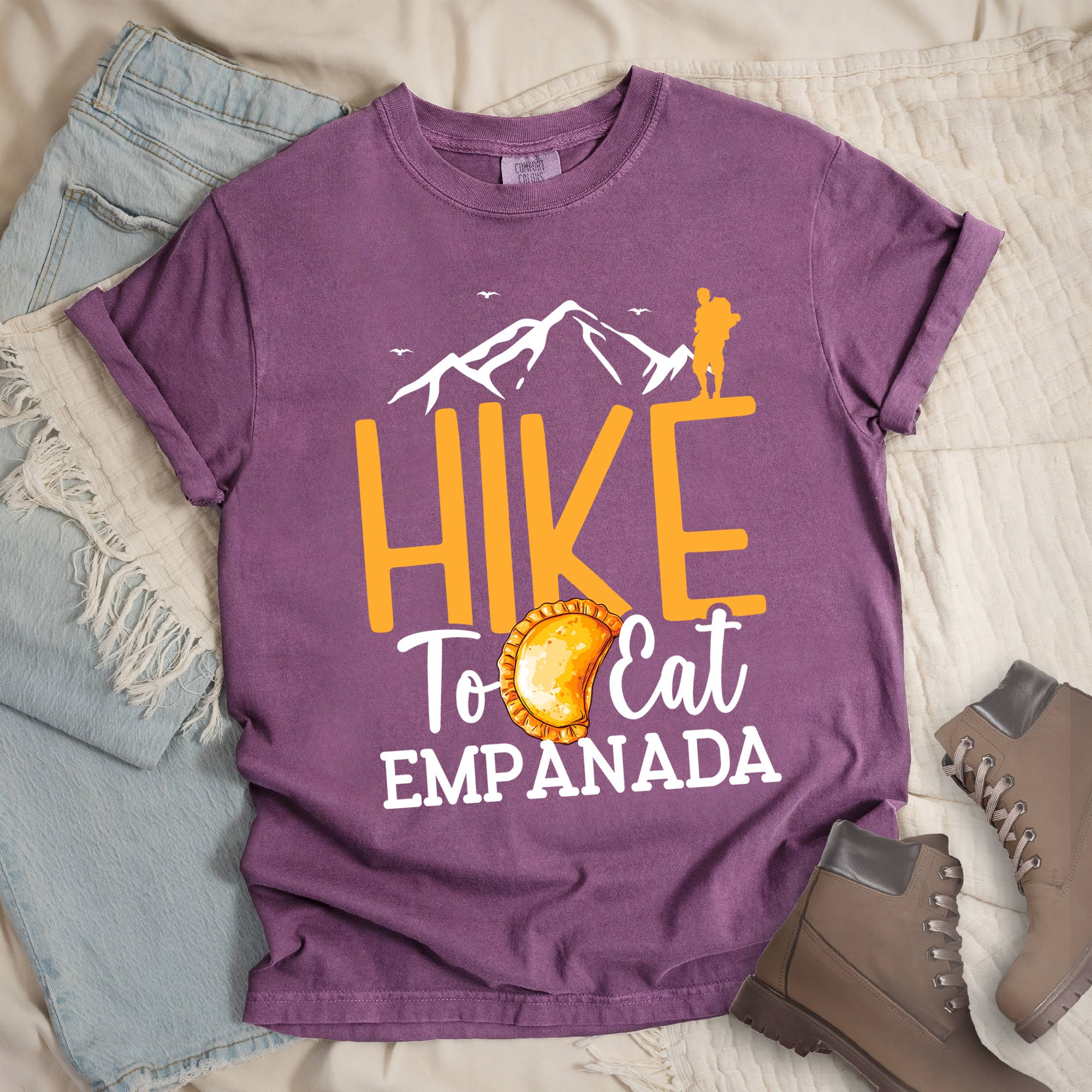 Dark pink shirt with Hiking Design featuring the phrase “Hike to Eat Empanada” and a hiker silhouette above a plate of empanada.