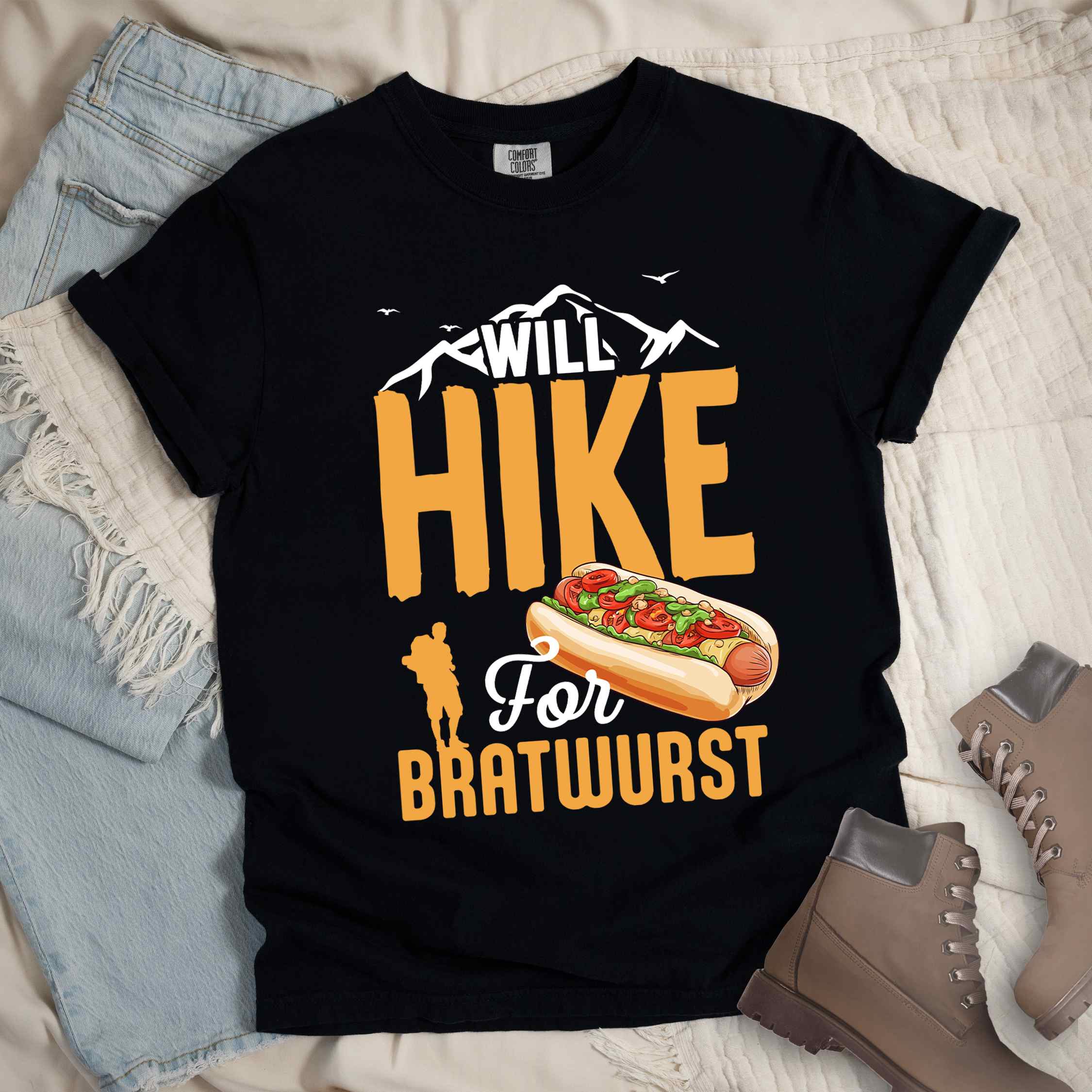 Black "Will hike for bratwurst" colored vintage tee with bold typography, illustrated bratwurst in a bun, mountains, birds, and backpackers for street food enthusiasts.
