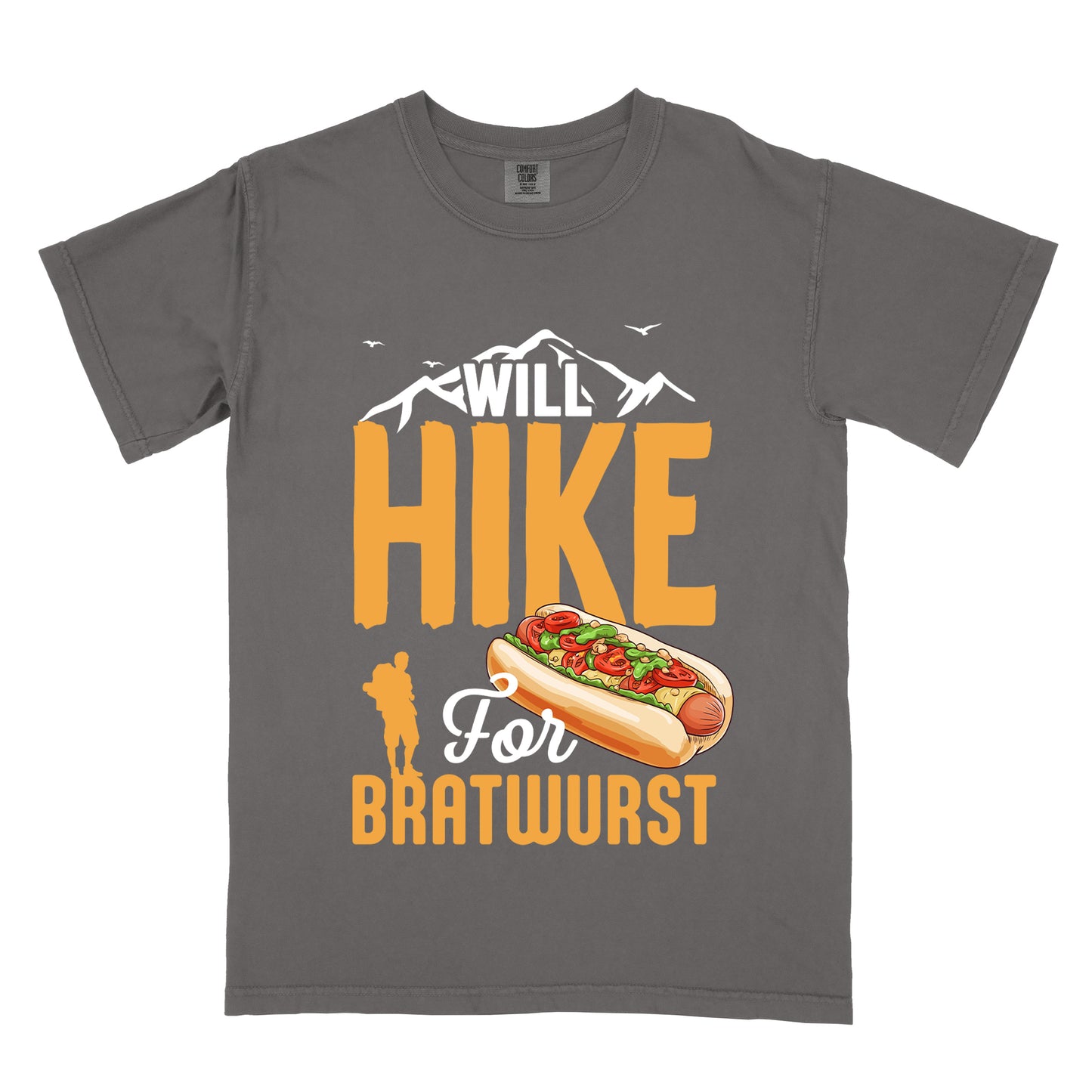 Pepper (Dark Gray) t-shirt with white, golden orange, and white text reading "WILL HIKE For BRATWURST". "WILL" appears in white text integrated with mountain outlines at the top, "HIKE" in large golden orange letters in the middle, "For" in white script below it, and "BRATWURST" in golden orange at the bottom. Features an illustration of a bratwurst in a bun with toppings to the right of "For" and a golden orange silhouette of a hiker to the left of "BRATWURST". Small white birds fly near the mountains.