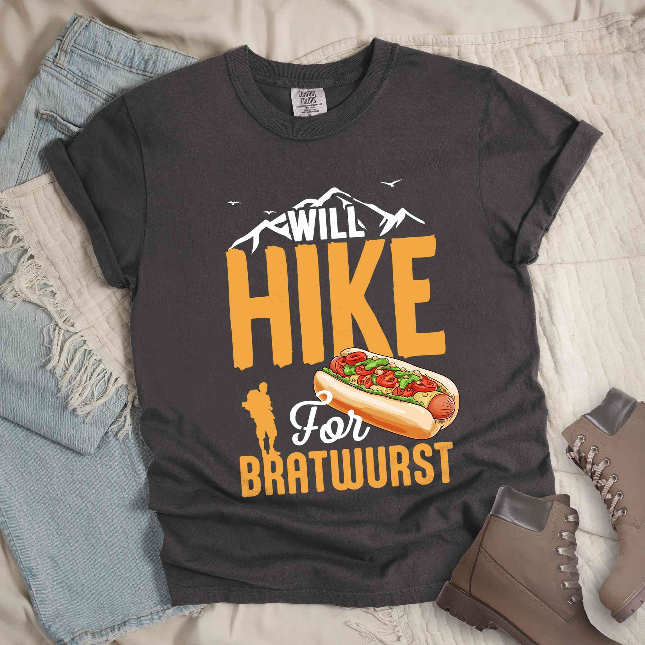 Pepper "Will hike for bratwurst" colored vintage tee with bold typography, illustrated bratwurst in a bun, mountains, birds, and backpackers for street food enthusiasts.