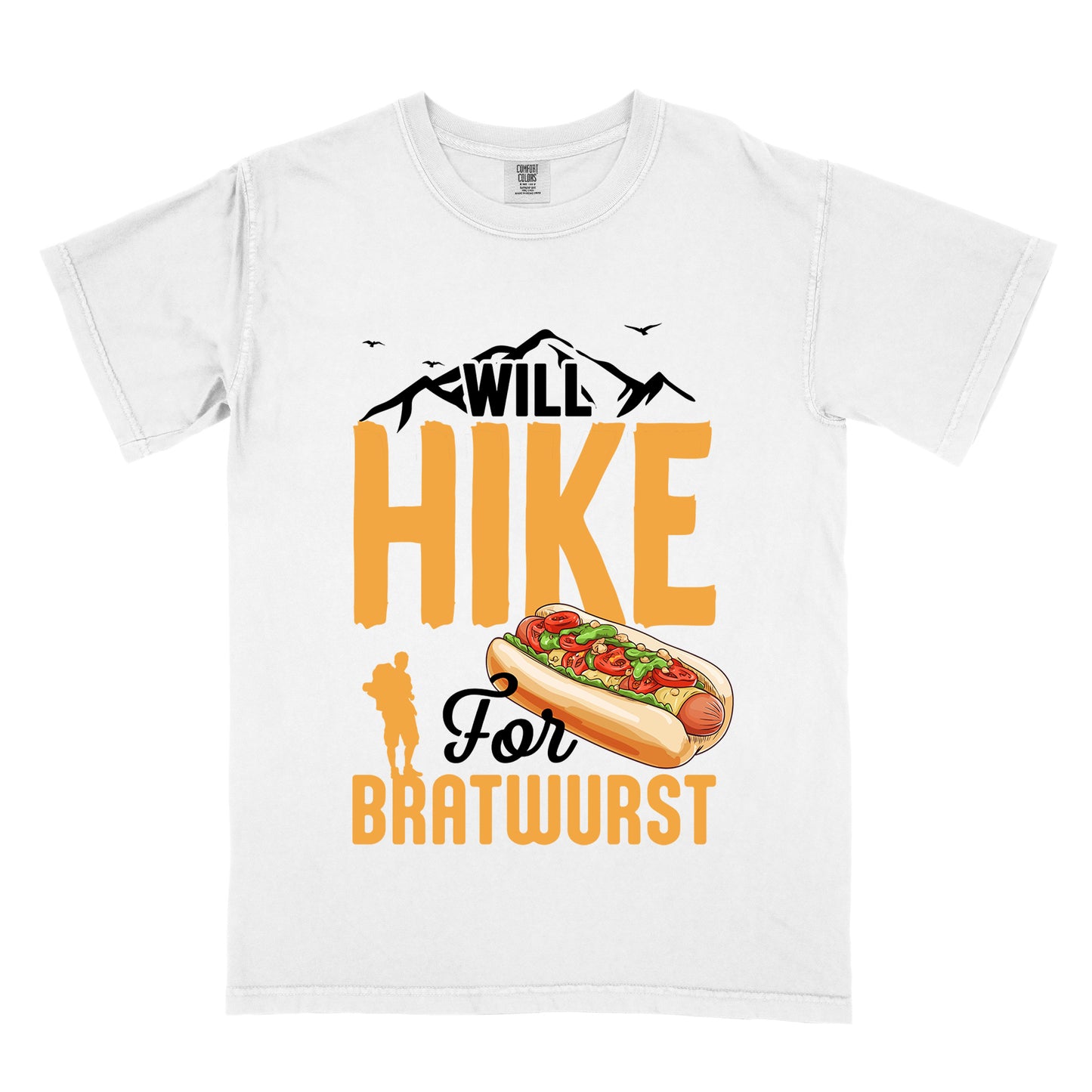 White t-shirt with black, golden orange, and black text reading "WILL HIKE For BRATWURST". "WILL" appears in black text integrated with mountain outlines at the top, "HIKE" in large golden orange letters in the middle, "For" in black script below it, and "BRATWURST" in golden orange at the bottom. Features an illustration of a bratwurst in a bun with toppings to the right of "For" and a golden orange silhouette of a hiker to the left of "BRATWURST". Small black birds fly near the mountains.