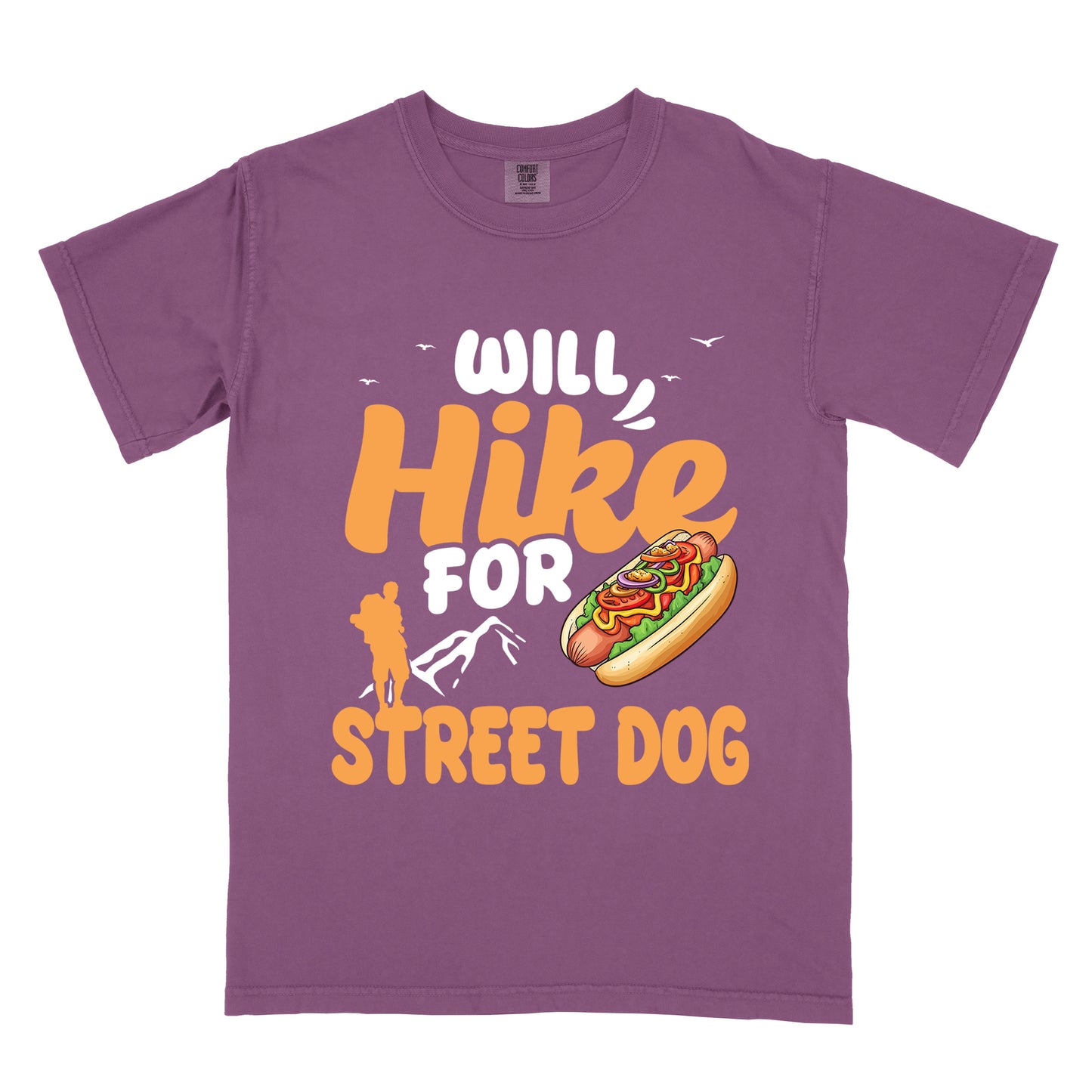 Berry (Dark Violet) t-shirt with orange and white text reading "WILL Hike FOR STREET DOG". "WILL" appears in white at the top with small white birds flying nearby, "Hike" in large orange script in the middle, "FOR" in white below it with small white mountain outlines, and "STREET DOG" in orange at the bottom. Features an illustration of a hot dog with toppings to the right of "FOR" and an orange silhouette of a hiker to the left top of "STREET DOG".