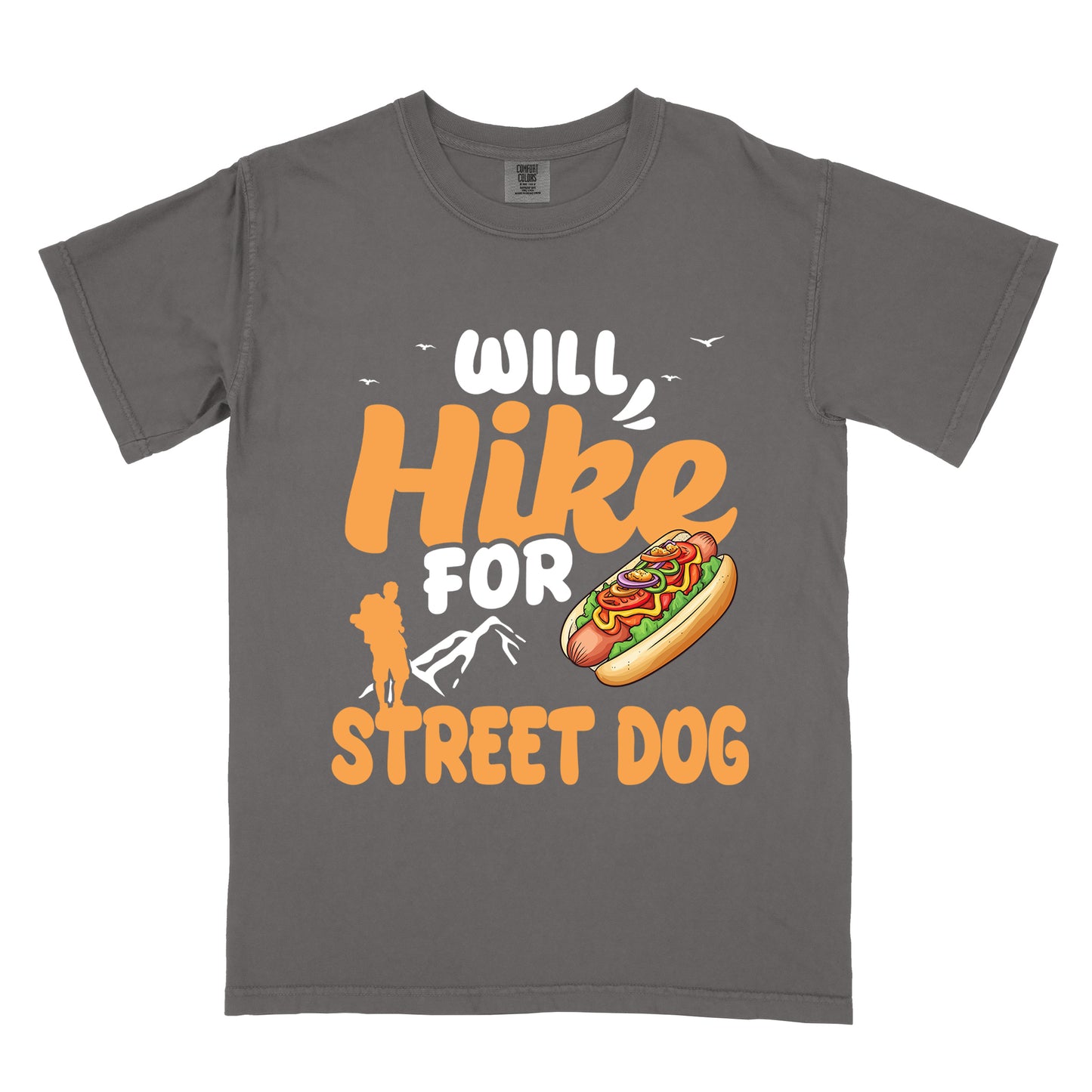 Pepper (Dark Gray) t-shirt with orange and white text reading "WILL Hike FOR STREET DOG". "WILL" appears in white at the top with small white birds flying nearby, "Hike" in large orange script in the middle, "FOR" in white below it with small white mountain outlines, and "STREET DOG" in orange at the bottom. Features an illustration of a hot dog with toppings to the right of "FOR" and an orange silhouette of a hiker to the left top of "STREET DOG".