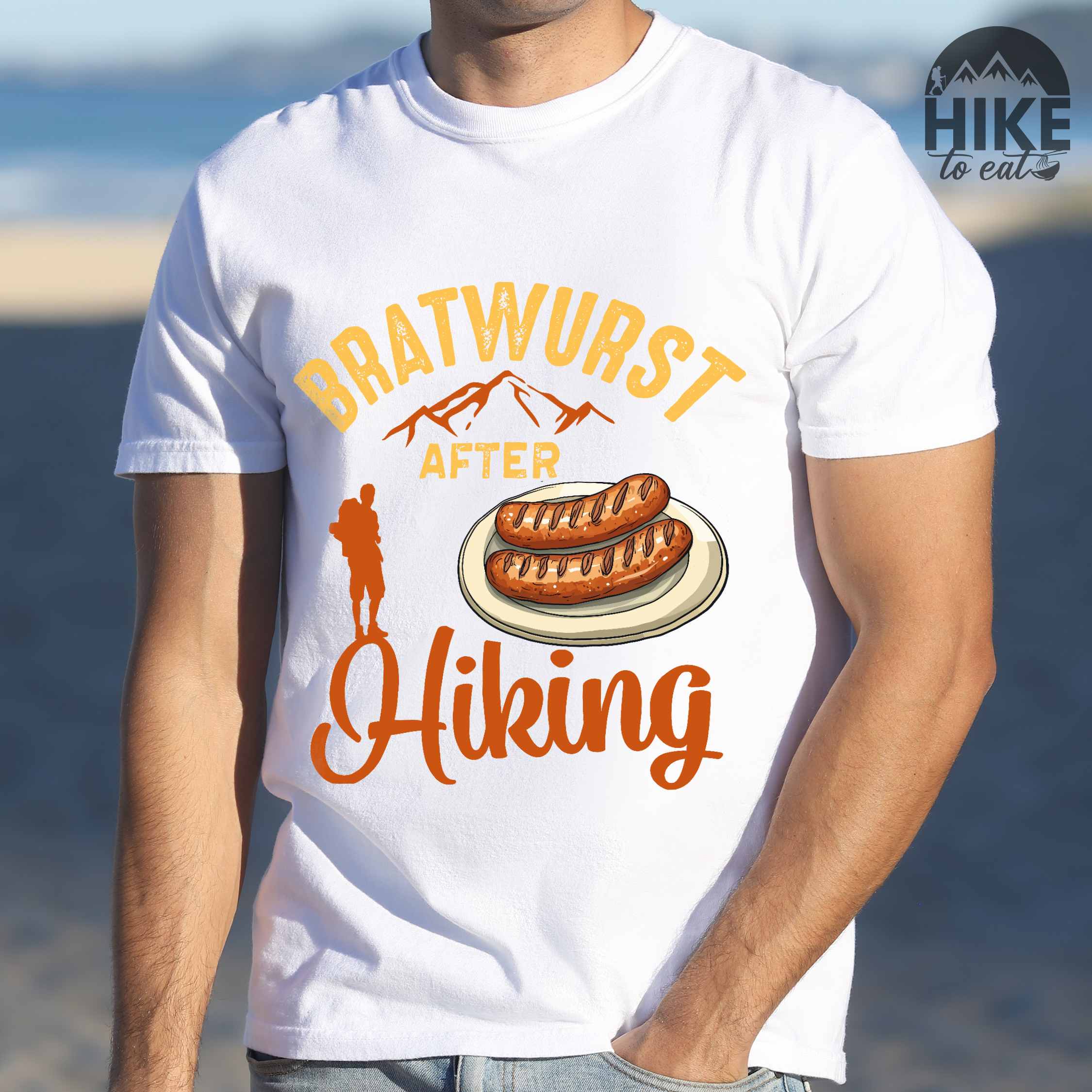 Man wearing white "bratwurst after hiking" colored vintage tee with bold typography, illustrated bratwurst on a plate, mountains, birds, and backpackers for street food enthusiasts.