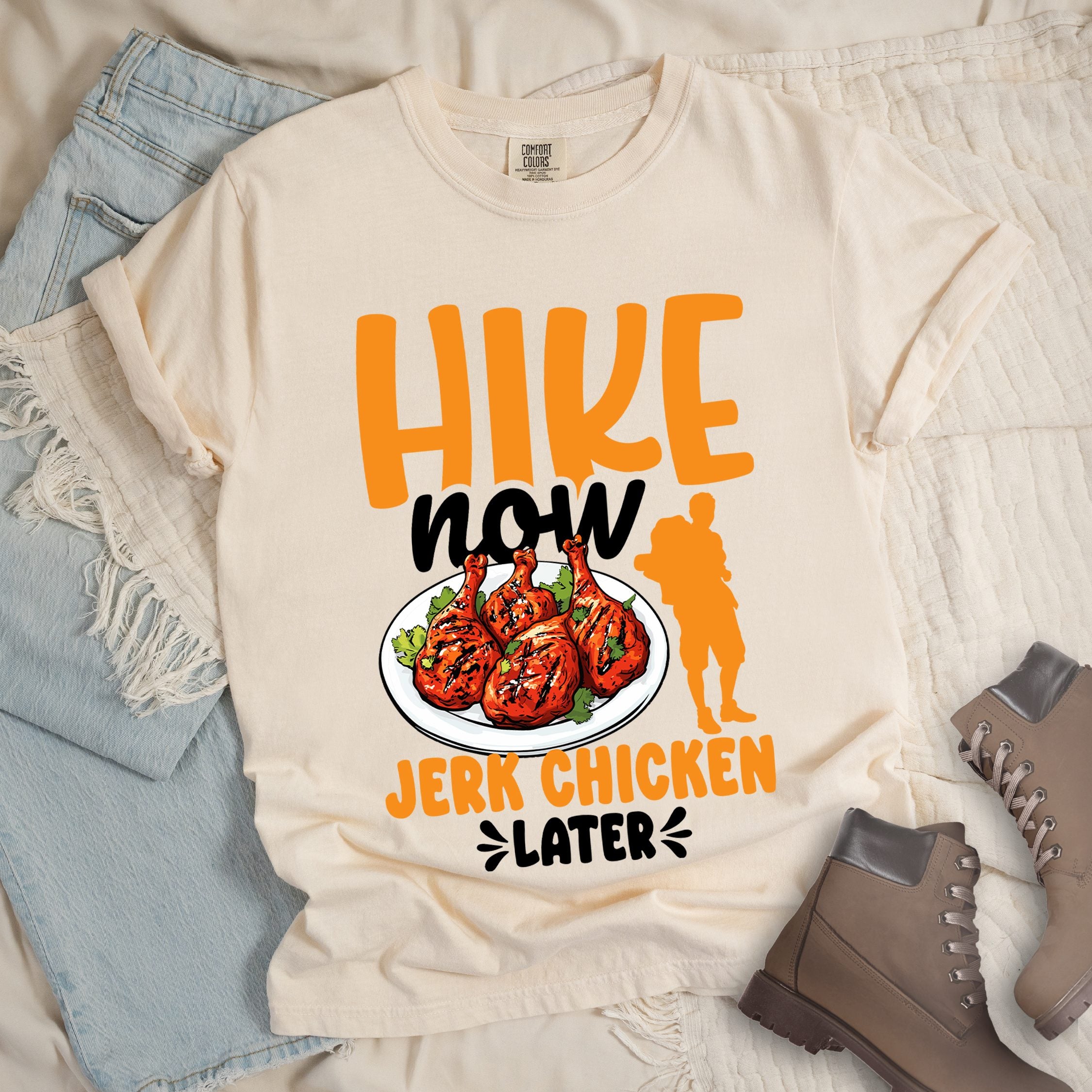 Ivory shirt with Hiking Design featuring the phrase “Hike Now Jerk Chicken Later” and an illustration of jerk chicken drumsticks.