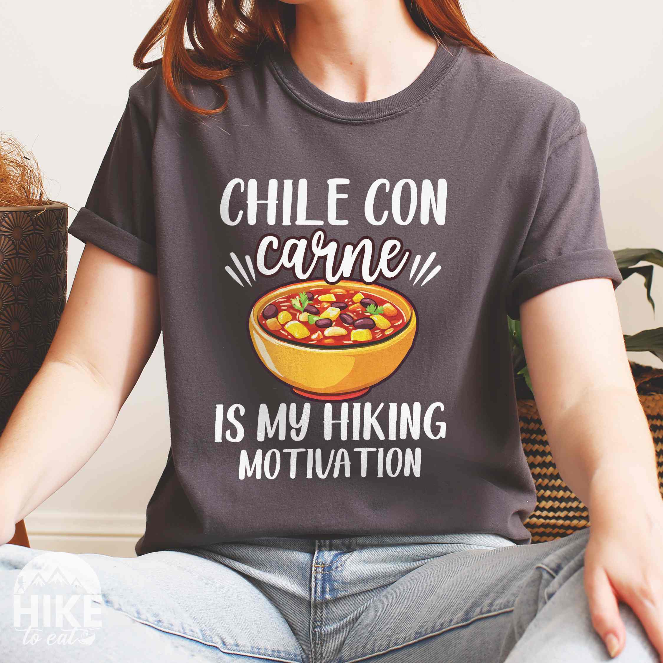 Woman wearing Pepper Chile con carne is my Hiking Motivation statement tee with bold typography, script lettering, and colorful chili bowl illustration for comfort food-loving outdoor enthusiasts