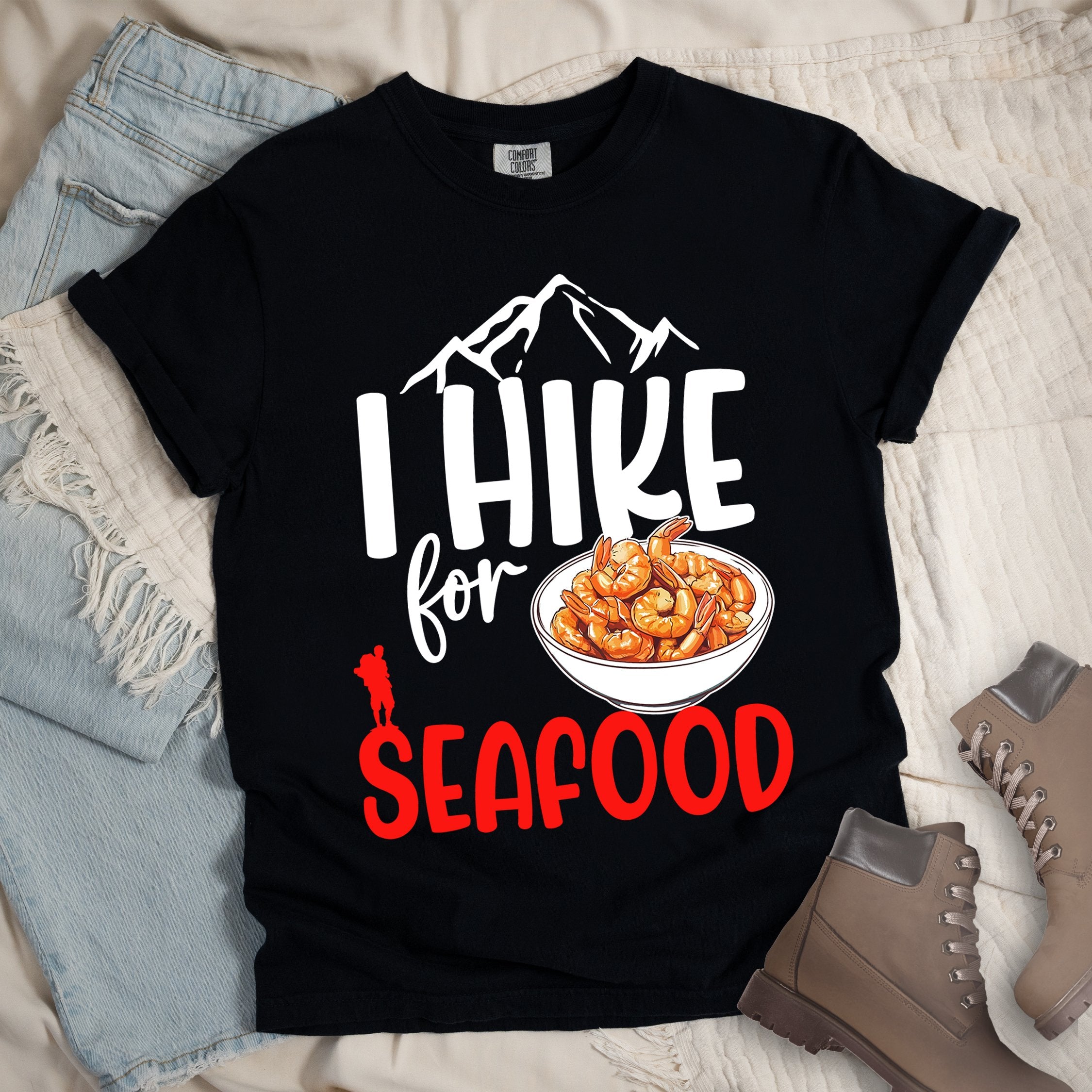 Black shirt with Hiking Design featuring the phrase “I Hike for Seafood” and an illustration of a bowl of shrimp with a hiker silhouette.