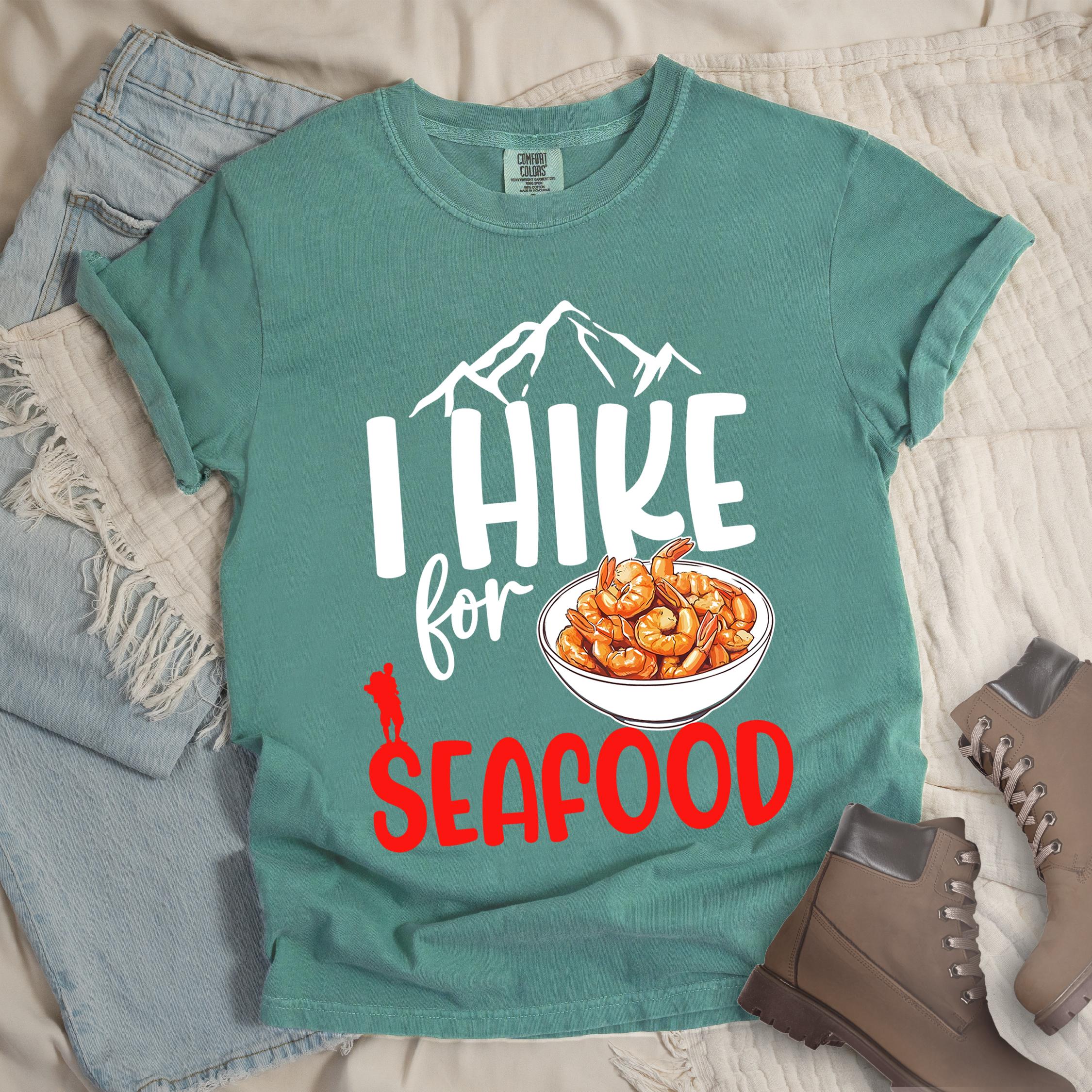 Green shirt with Hiking Design featuring the phrase “I Hike for Seafood” and an illustration of a bowl of shrimp with a hiker silhouette.
