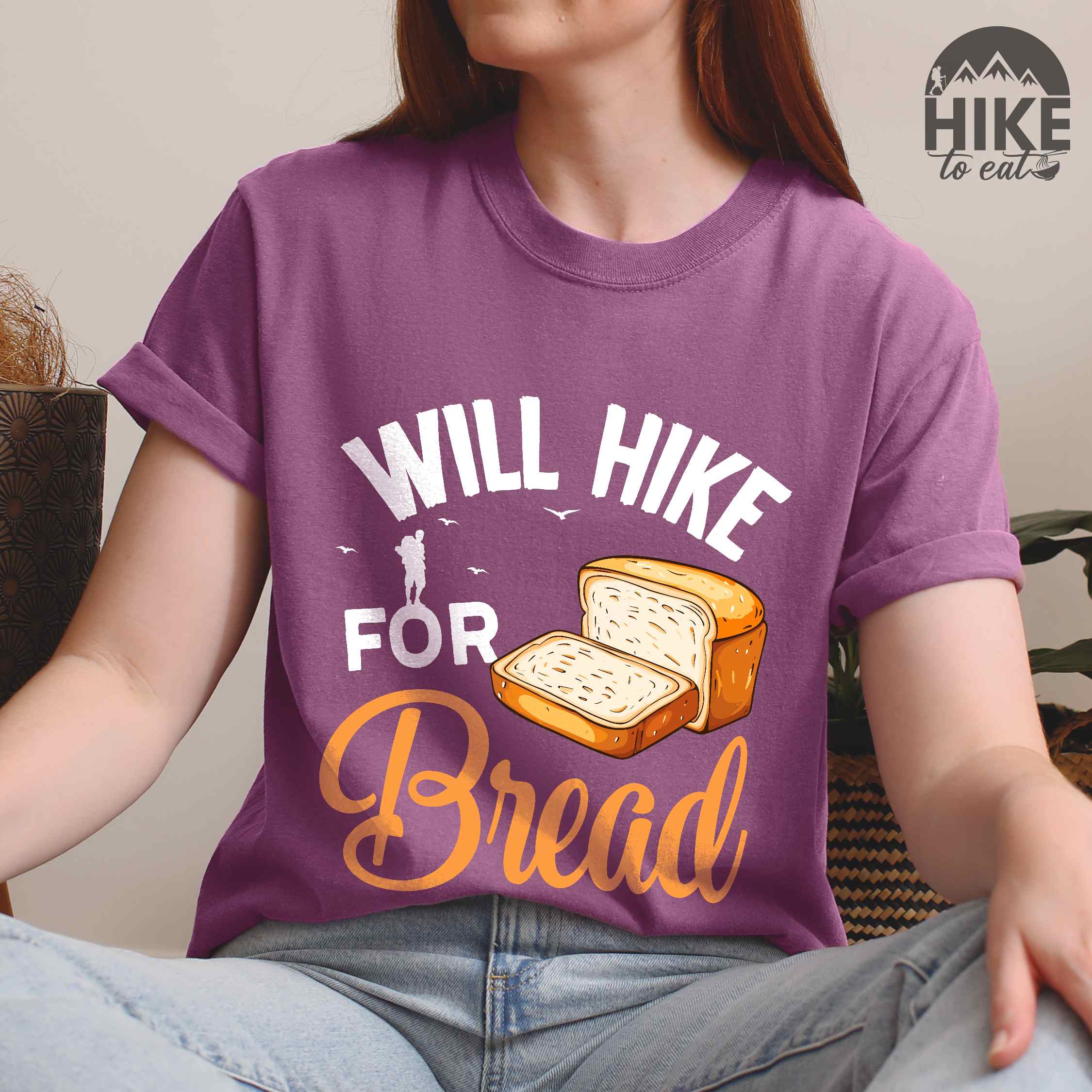 Woman wearing berry "Will hike for bread" colored statement tee with flowing script typography, bold lettering, and loaf of bread illustration for pastry-loving outdoor enthusiasts, hikers and foodies