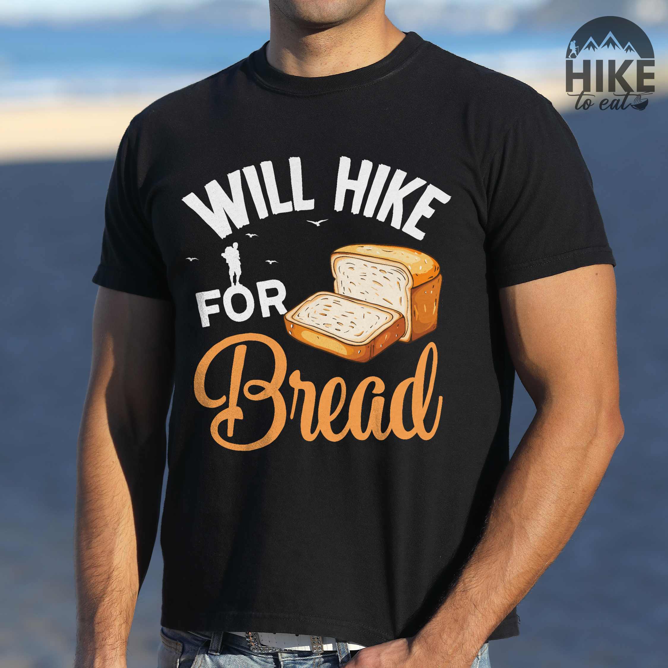 Man wearing black "Will hike for bread" colored statement tee with flowing script typography, bold lettering, and loaf of bread illustration for pastry-loving outdoor enthusiasts, hikers and foodies