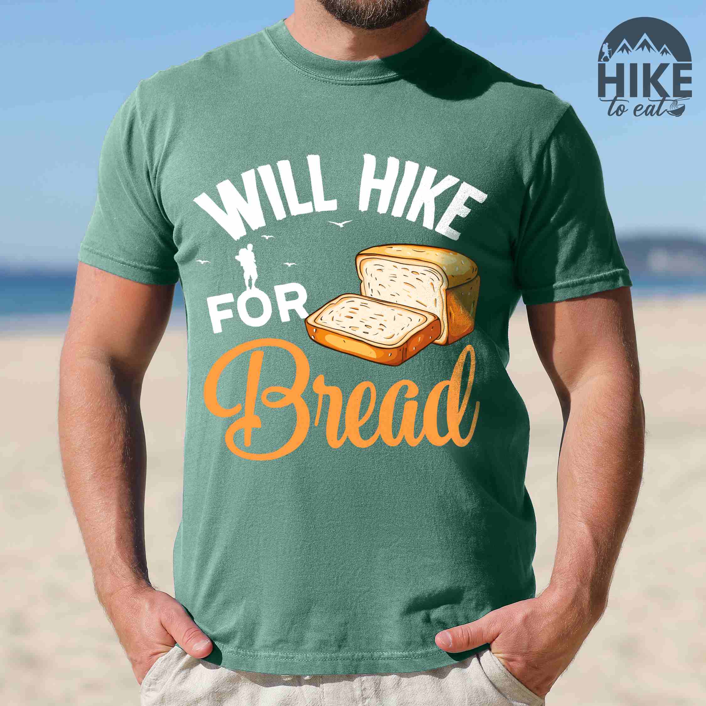 Man wearing light green "Will hike for bread" colored statement tee with flowing script typography, bold lettering, and loaf of bread illustration for pastry-loving outdoor enthusiasts, hikers and foodies