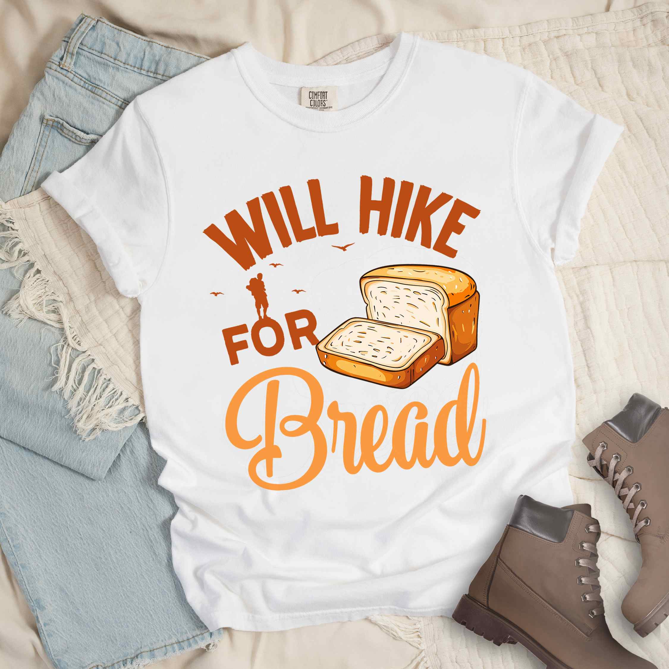 White "Will hike for bread" colored statement tee with flowing script typography, bold lettering, and loaf of bread illustration for pastry-loving outdoor enthusiasts, hikers and foodies