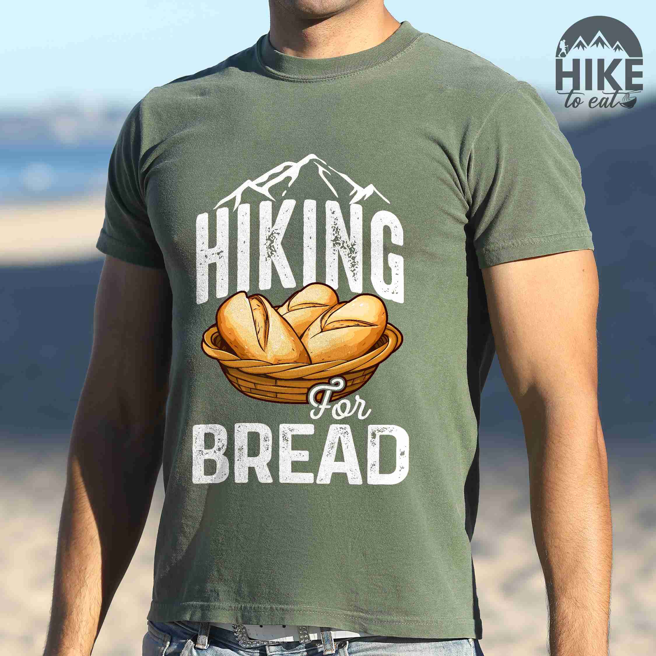 Man wearing moss "Hiking for bread" colored statement tee with flowing script typography, bold lettering, and freshly baked bread illustration for pastry-loving outdoor enthusiasts, hikers and foodies