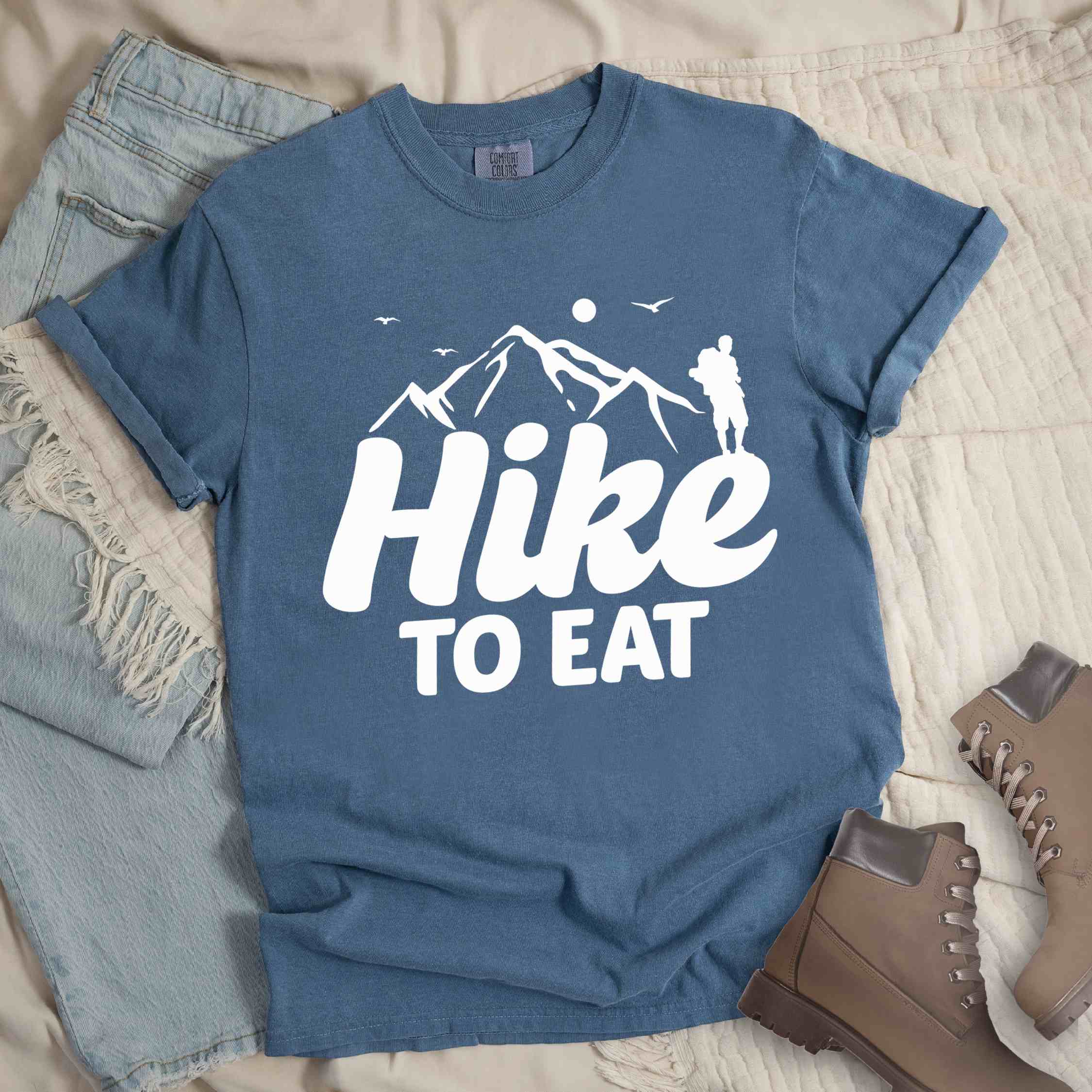 blue jean "Hike to Eat" colored statement tee with bold typography, mountains, birds, sunrise, perfect for food motivated individuals.