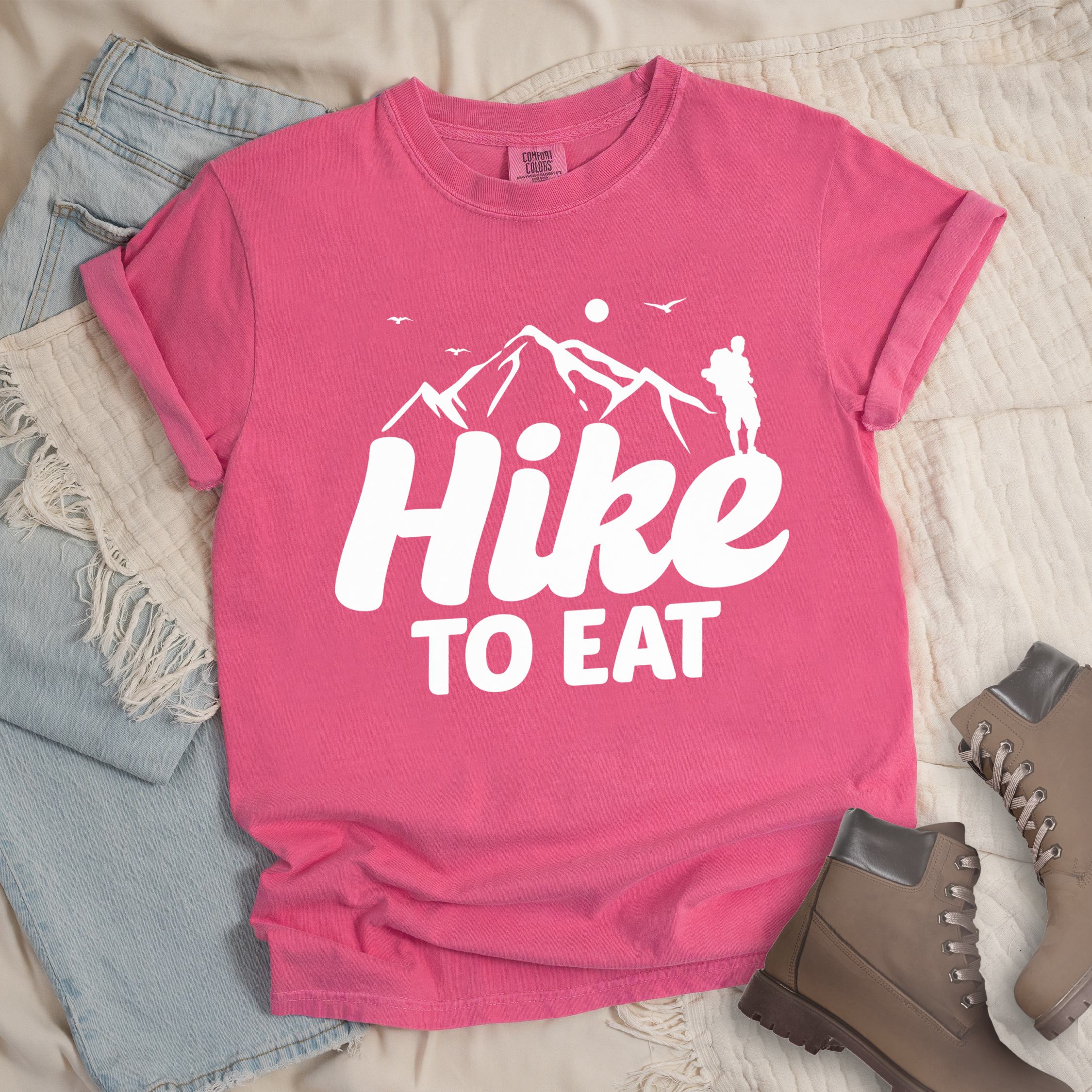 Pink shirt with Hiking Design featuring the phrase “Hike To Eat” showing a hiker silhouette and mountain illustration.