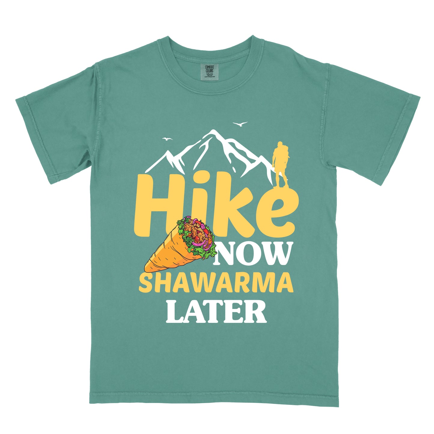 Light Green t-shirt with text "HIKE NOW SHAWARMA LATER" in yellow and white lettering. A mountain silhouette appears above with a small hiker figure. The word "HIKE" is in large yellow text, "NOW" in smaller white text, "SHAWARMA" in yellow with an illustration of a shawarma wrap beside it, and "LATER" in white. The design emphasizes hiking motivation with food reward.