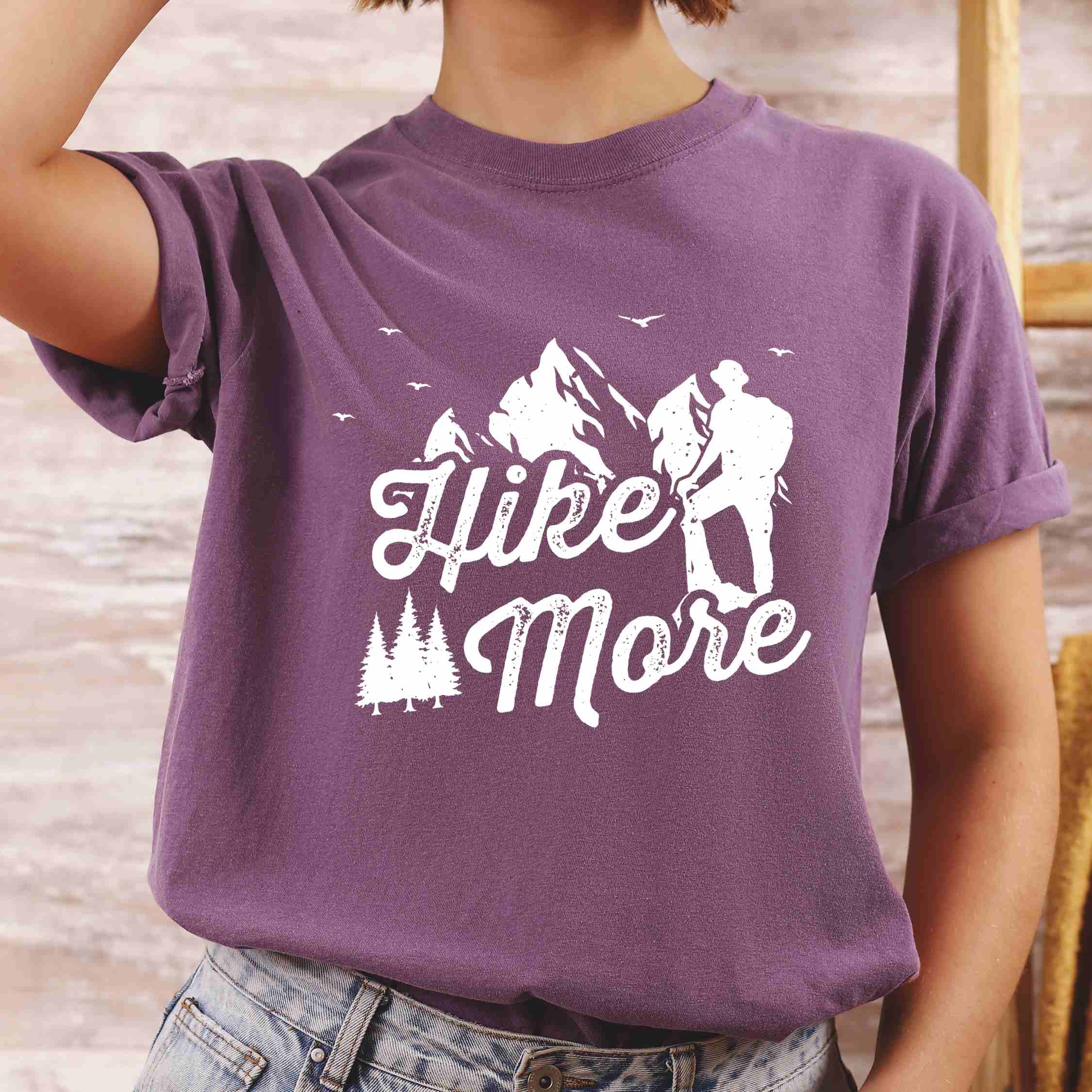 woman wearing berry "Hike More" colored statement tee with bold typography, mountains, birds, perfect for food motivated individuals.