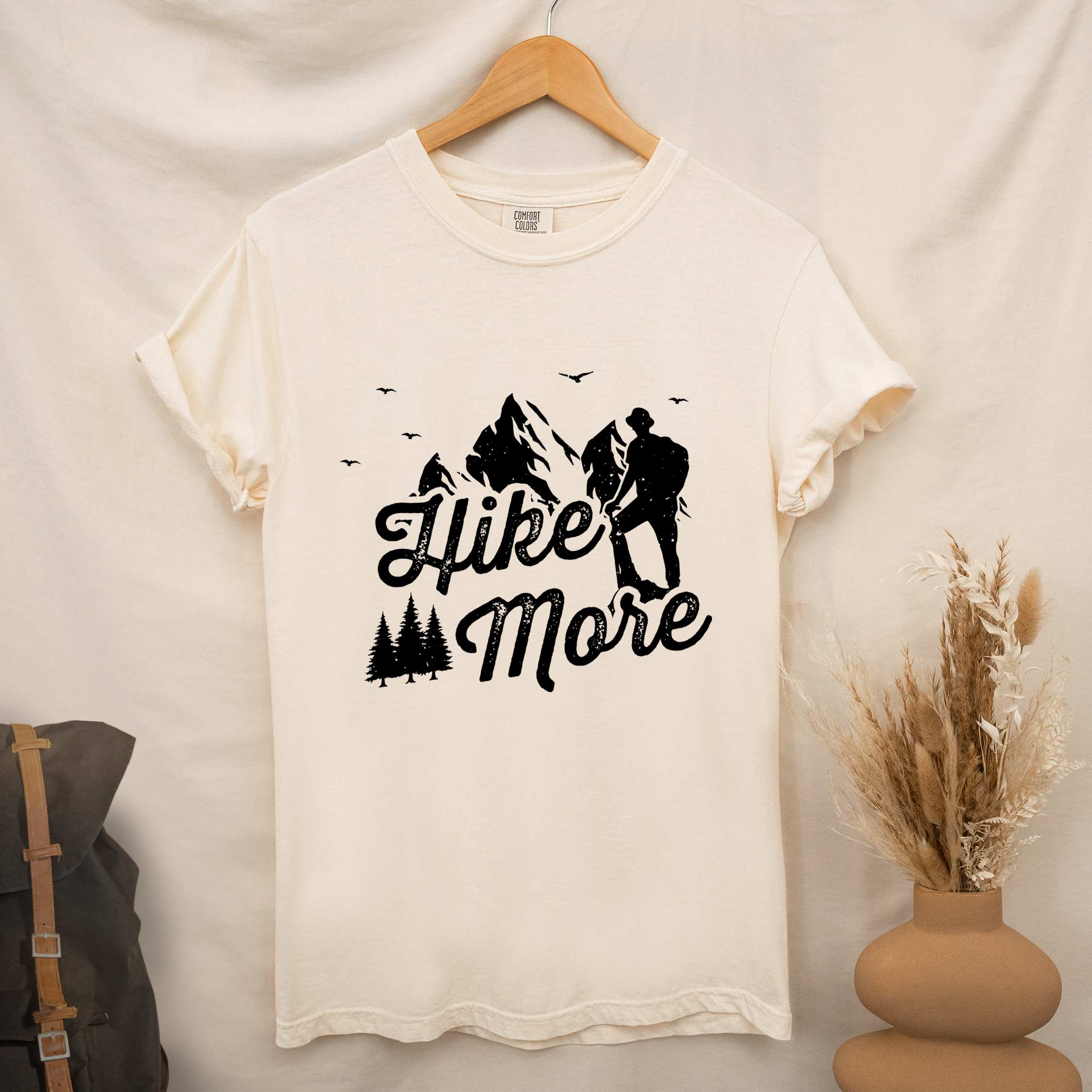 Hanging ivory "Hike More" colored statement tee with bold typography, mountains, birds, perfect for food motivated individuals.
