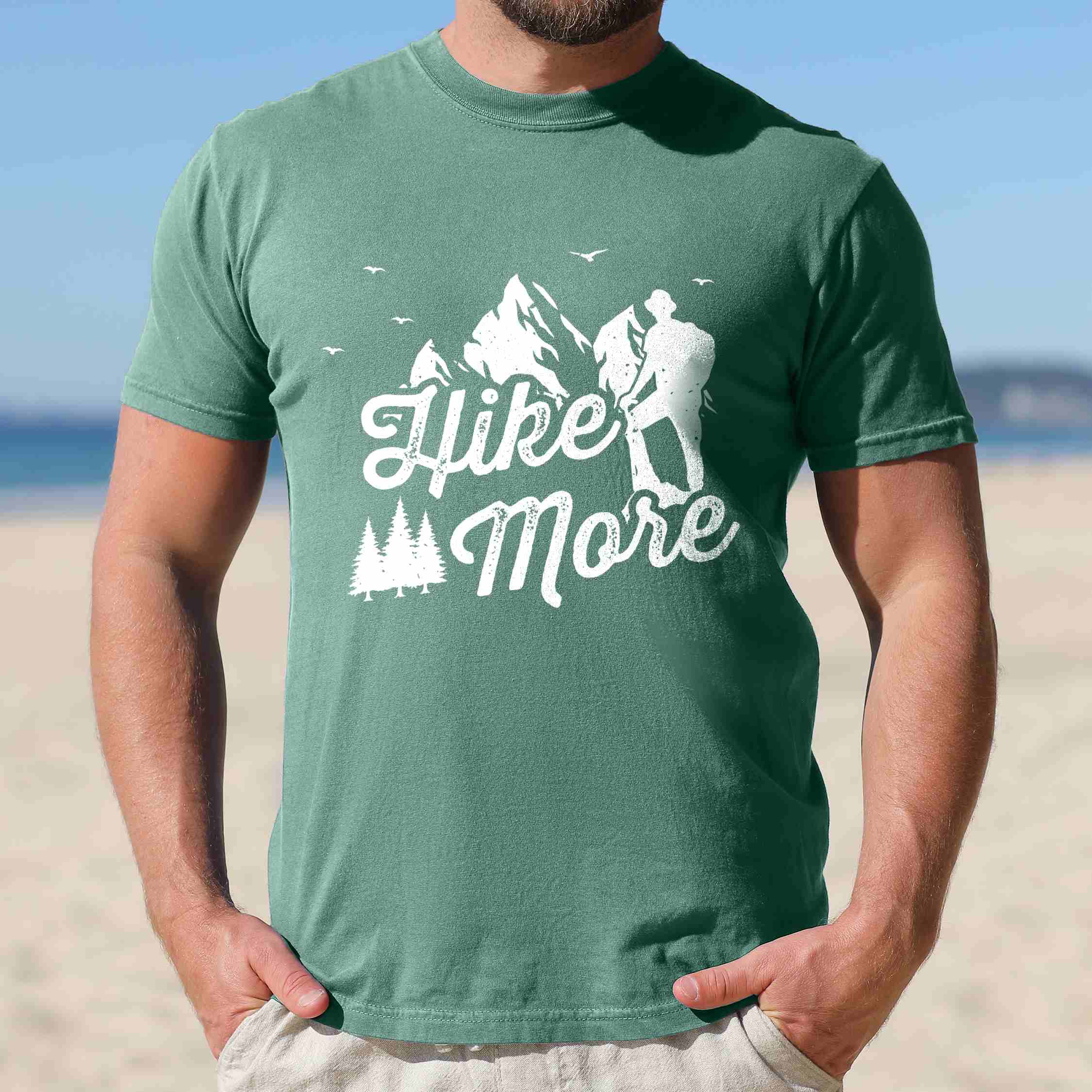 Man wearing light green "Hike More" colored statement tee with bold typography, mountains, birds, perfect for food motivated individuals.