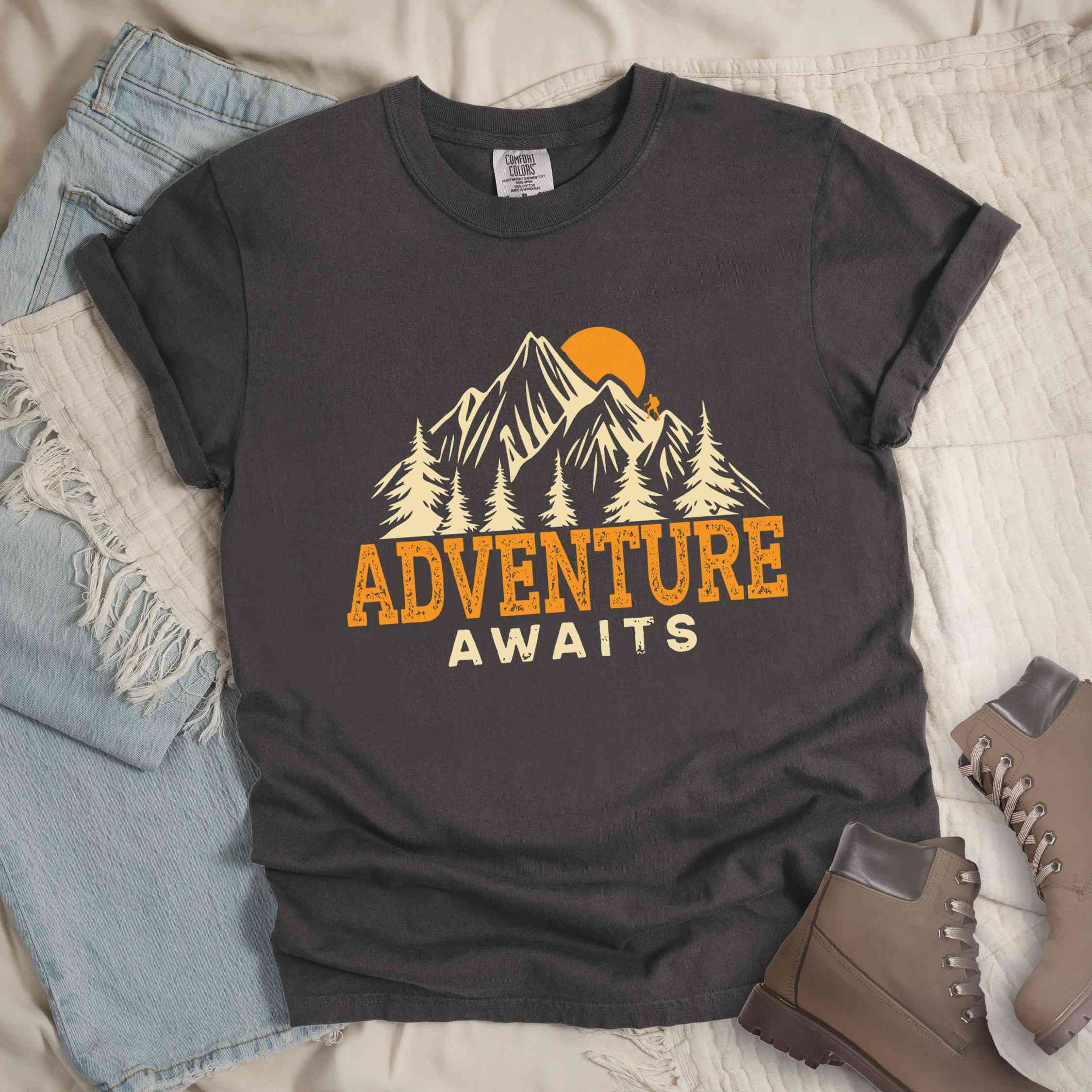 Pepper "Adventure Awaits" colored statement tee with bold typography, mountains, birds, perfect for adventure motivated individuals.