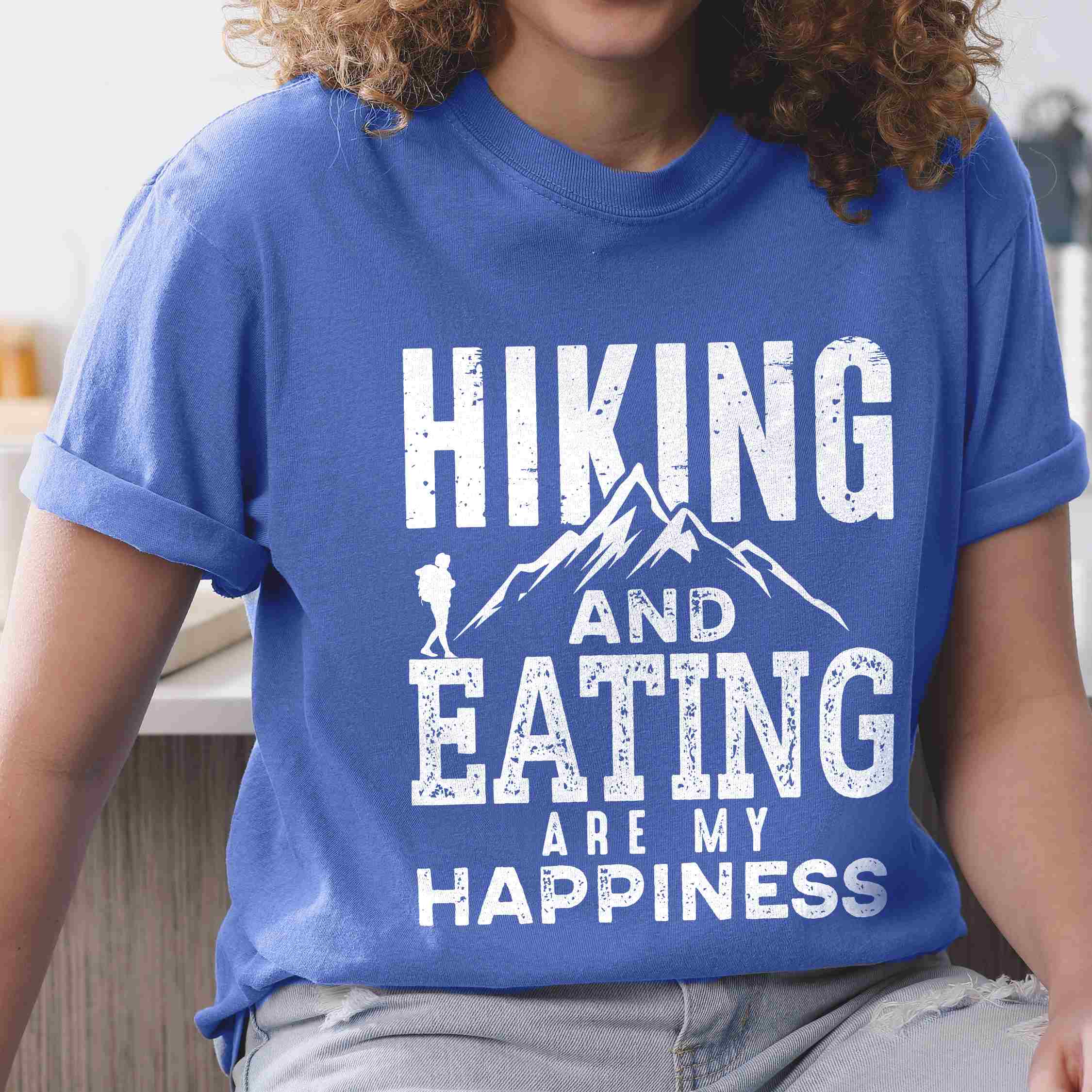 Woman wearing flo blue "Hiking and Eating are my happiness" colored statement tee with bold typography, mountains, birds, perfect for adventure motivated individuals.