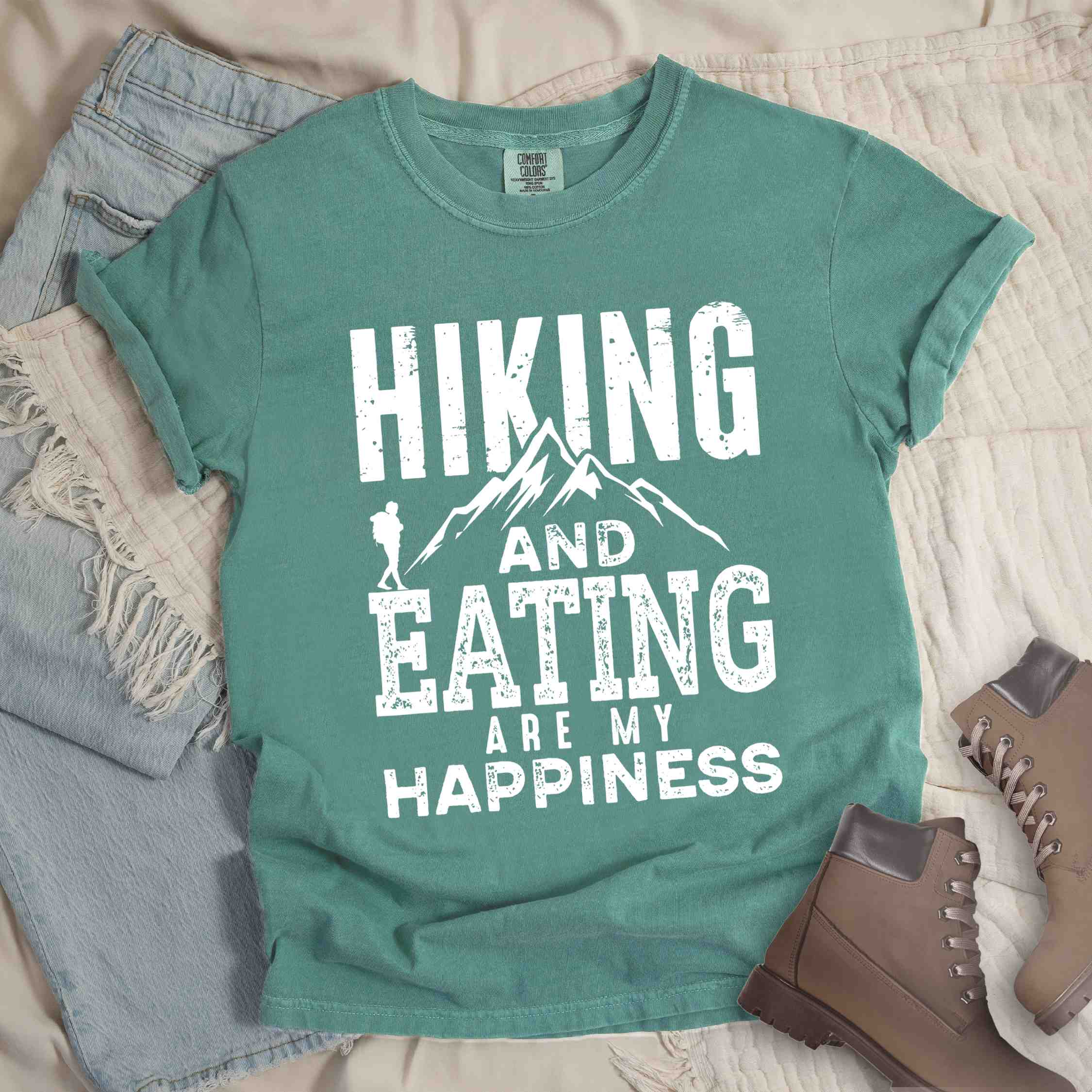 Light green "Hiking and Eating are my happiness" colored statement tee with bold typography, mountains, birds, perfect for adventure motivated individuals.