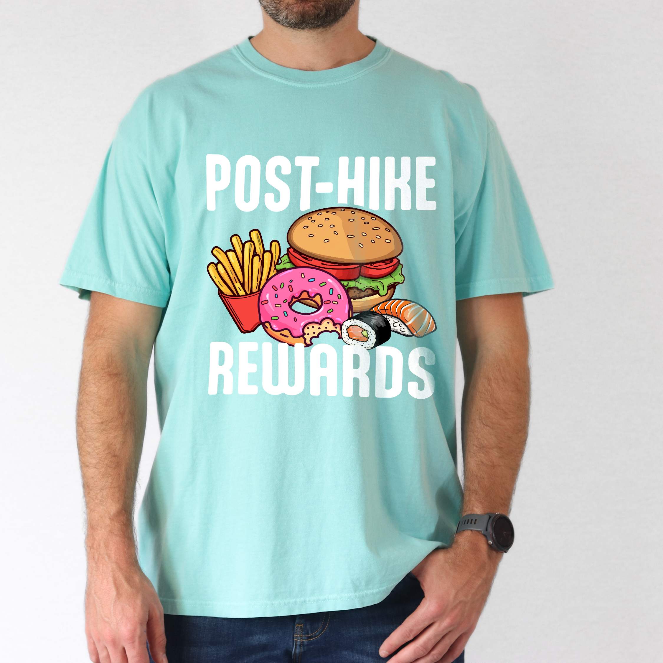 Man wearing chalky mint "Post-hike rewards" colored statement tee with bold typography, mountains, birds, illustrated fast food meal, perfect for adventure motivated individuals and looking for post-hike meal.