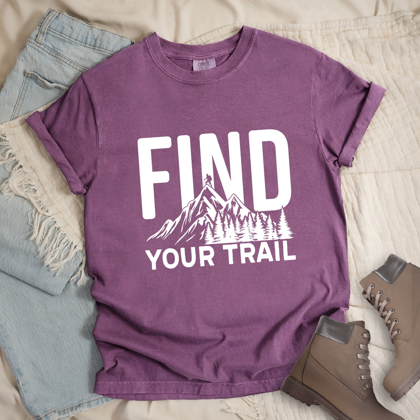 Berry (Dark Violet) graphic t-shirt with 'Find Your Trail' text and white mountain and forest design, styled with light wash jeans and brown hiking boots