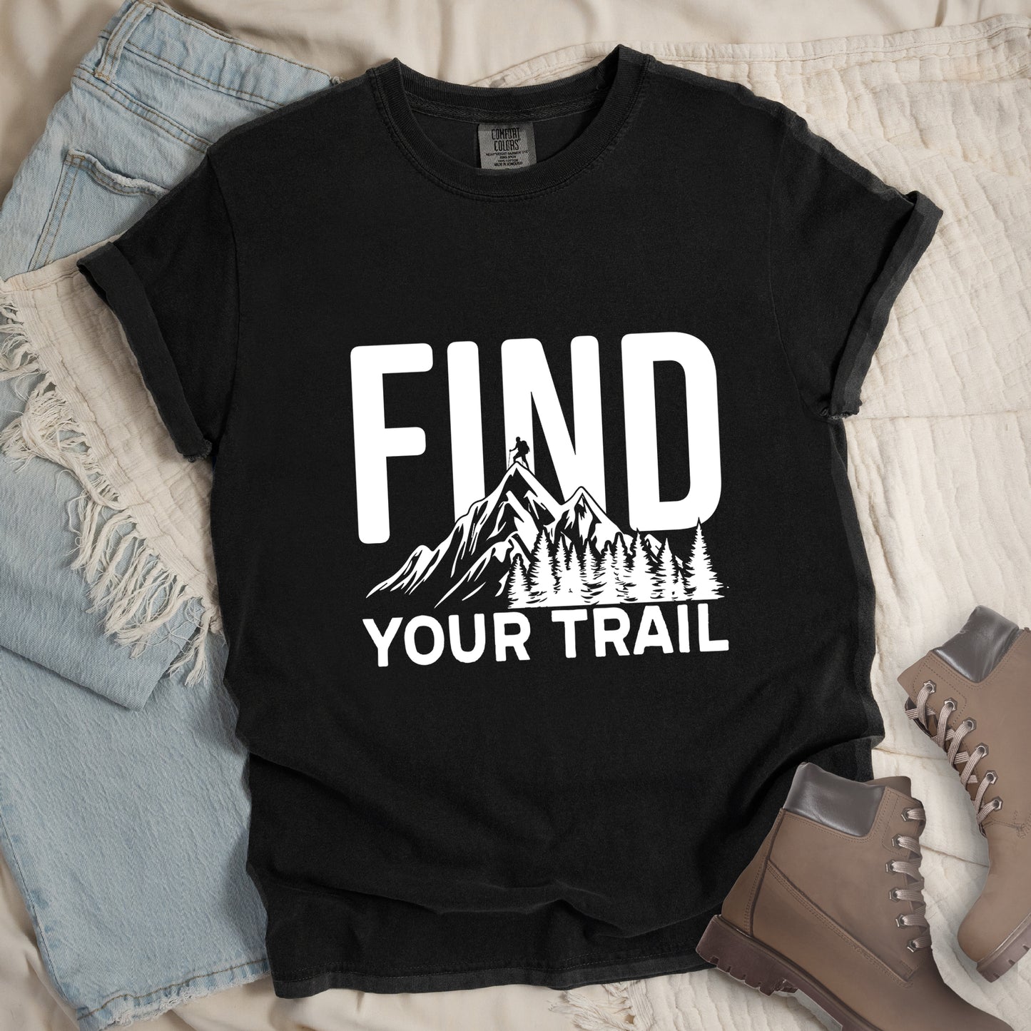 Black graphic t-shirt with 'Find Your Trail' text and white mountain and forest design, styled with light wash jeans and brown hiking boots